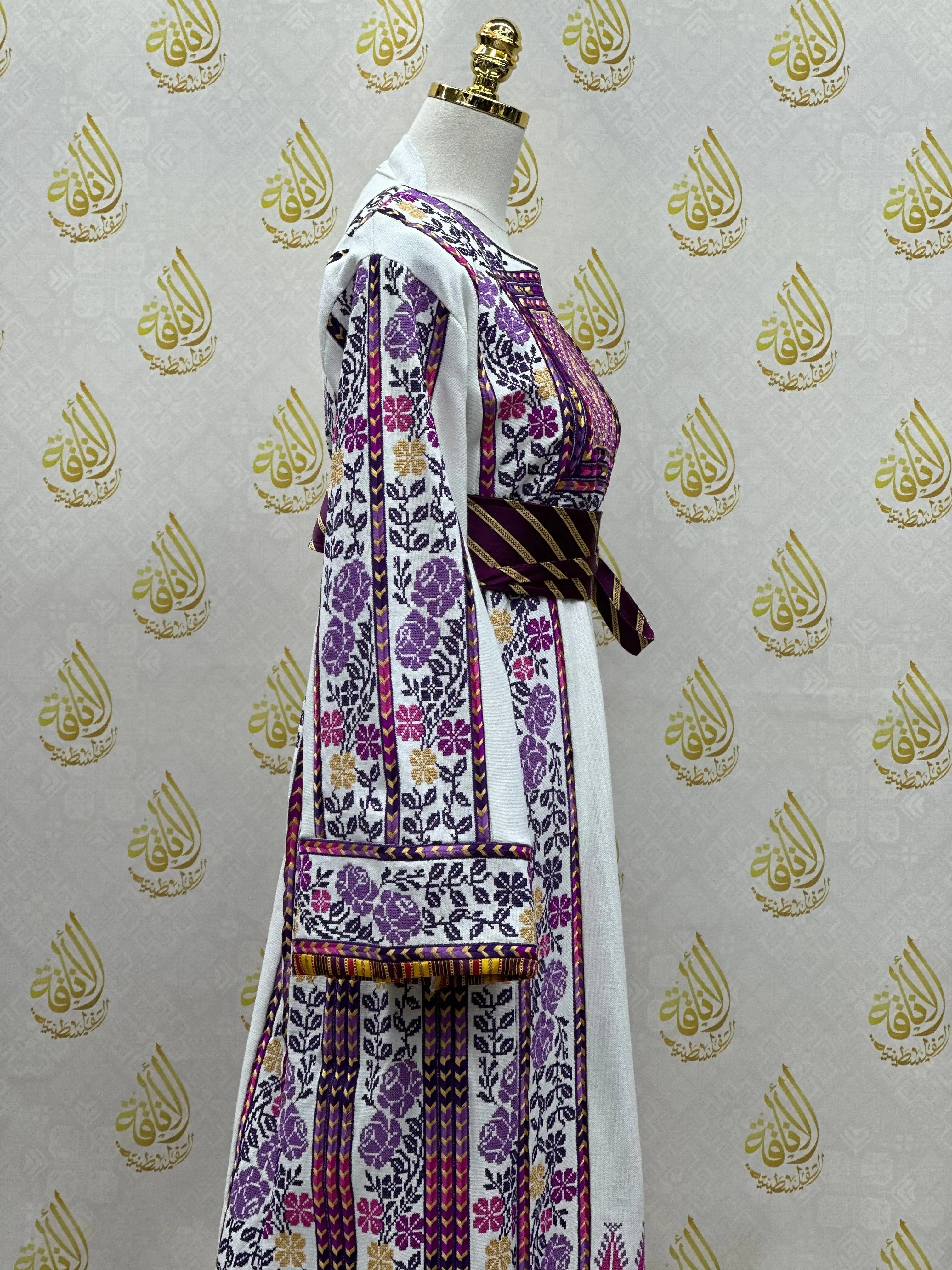 Palestinian Elegance purple and white Palestinian embroidered thobe with floral patterns and striped belt on mannequin