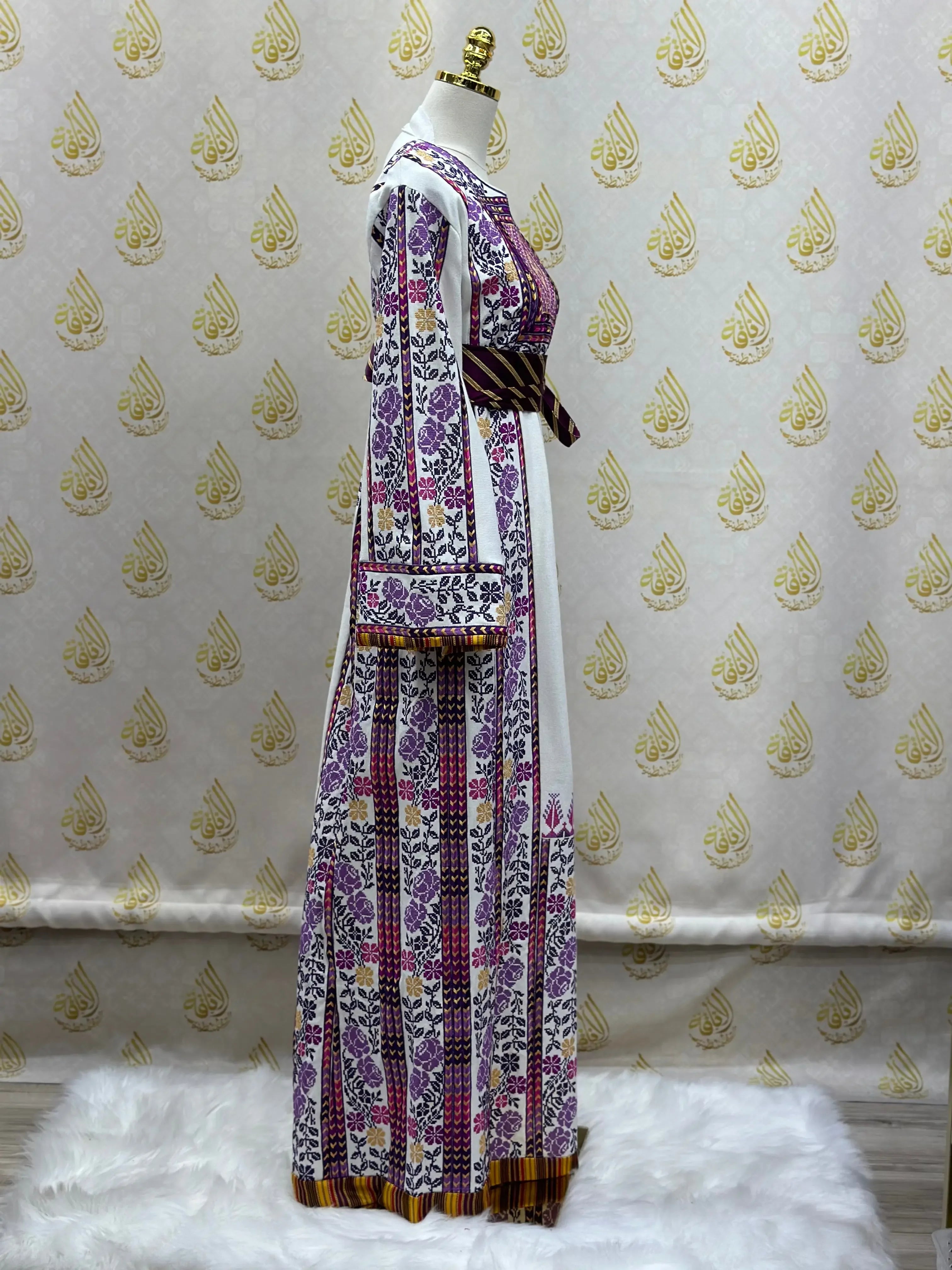 Palestinian embroidered thobe by Palestinian Elegance with intricate purple and pink floral patterns on white fabric