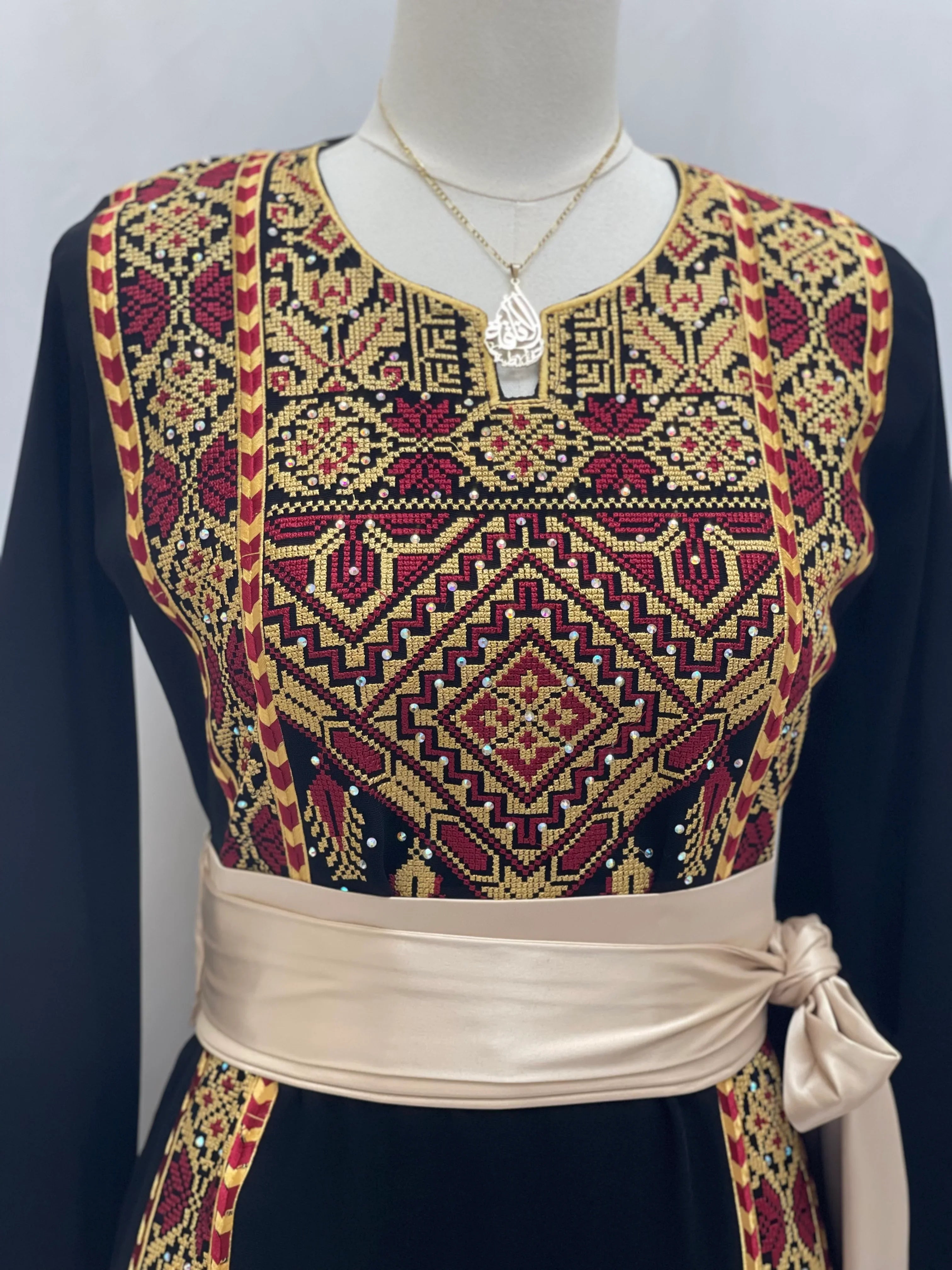 Palestinian embroidered thoub with intricate red and gold embroidery and a beige sash belt
