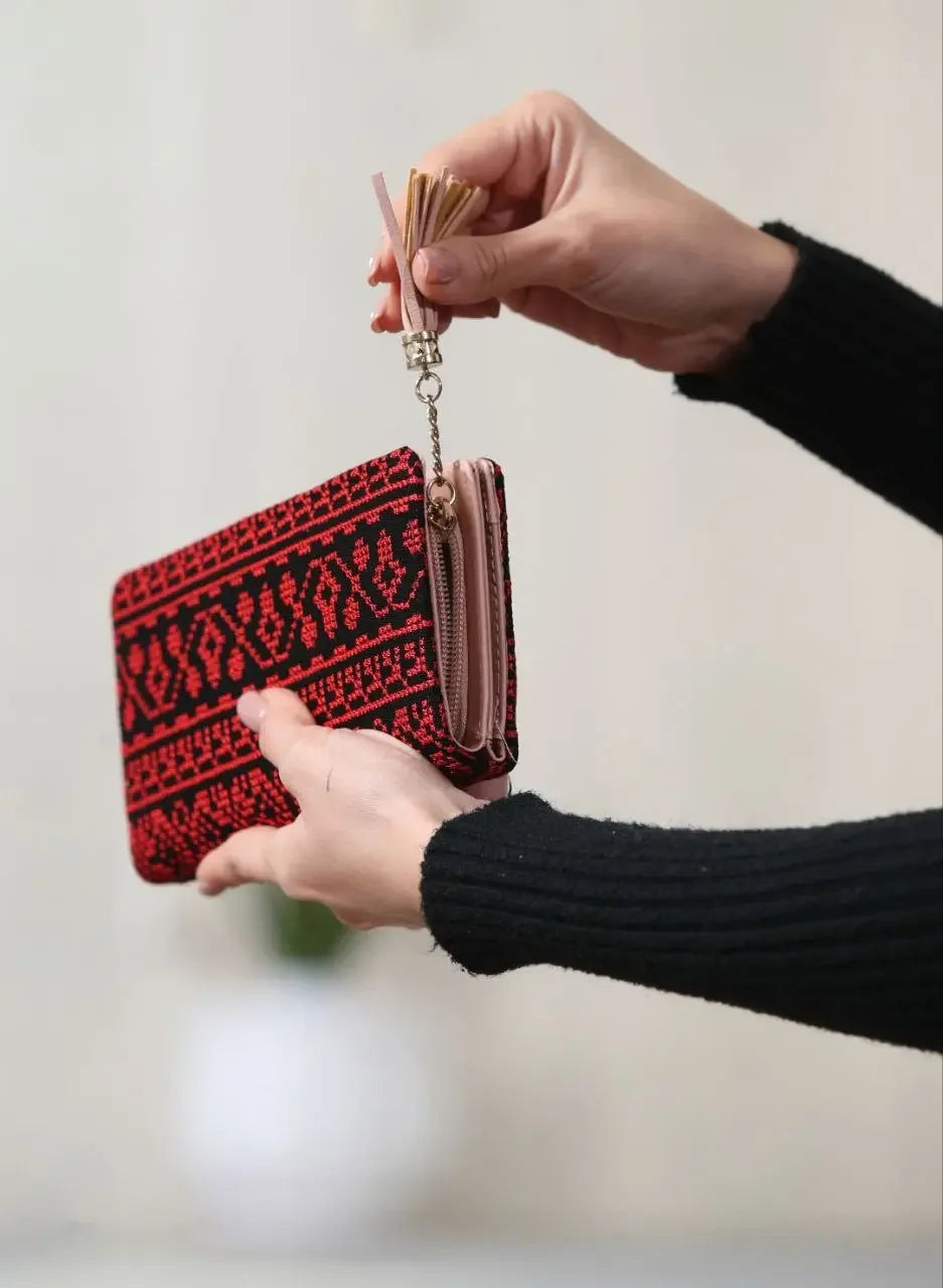 Palestinian embroidered wallet in red and black held by hands with tassel zipper from Palestinian Elegance