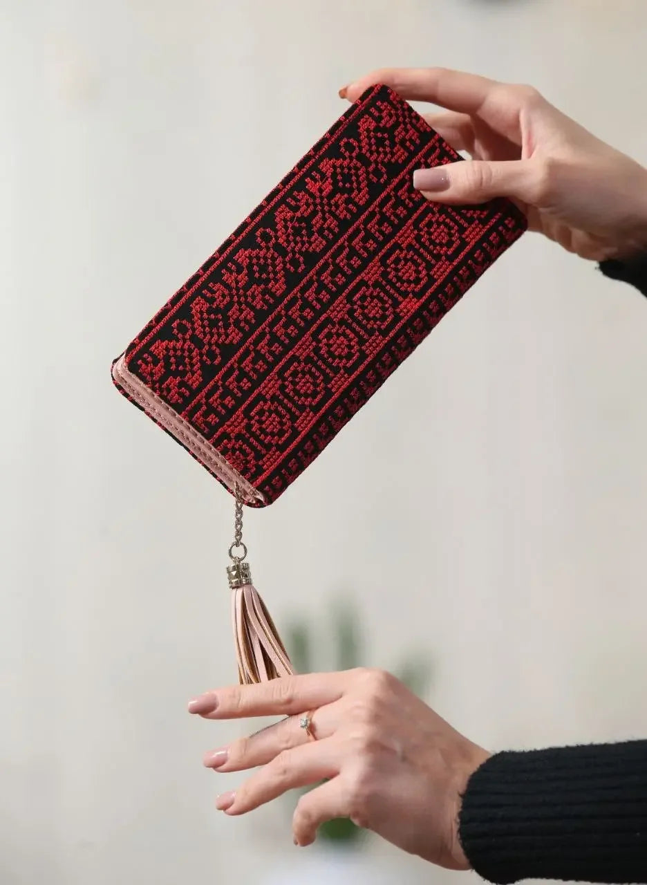 Palestinian embroidered wallet with red and black traditional patterns and tassel detail held by hands