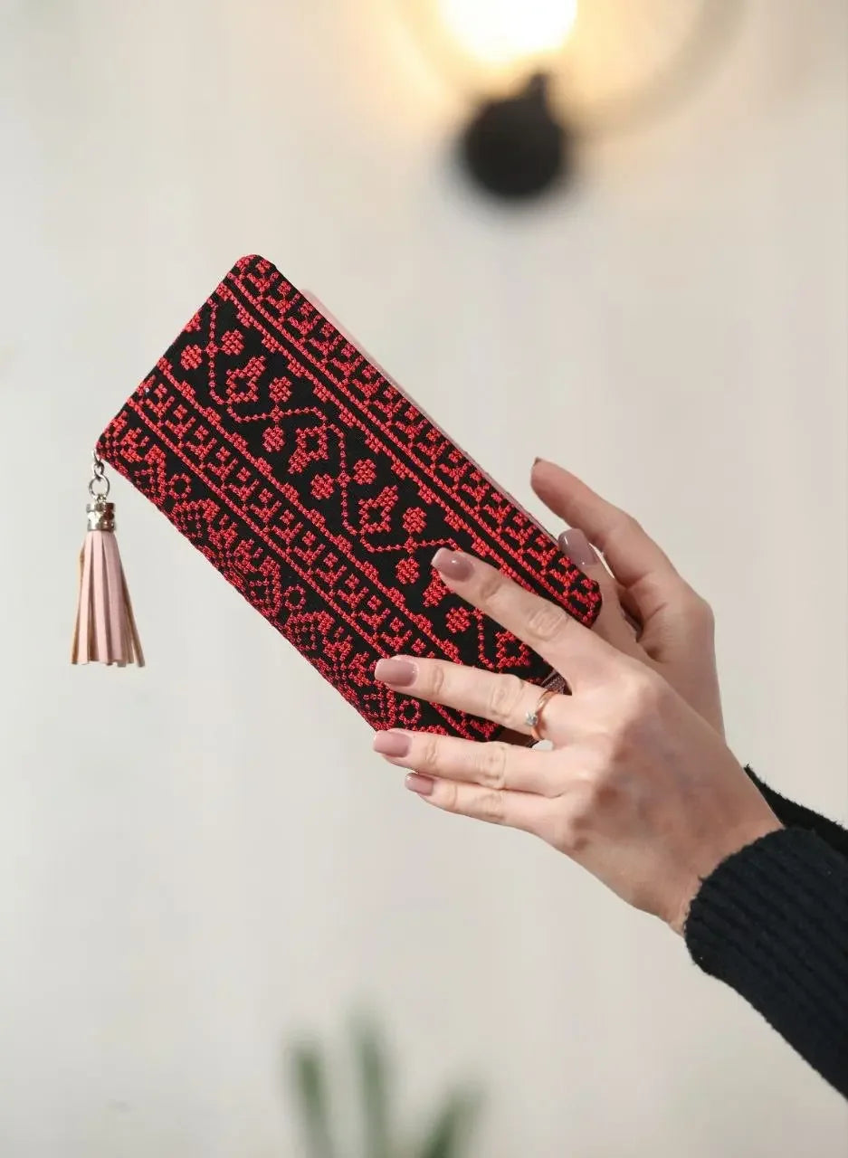 Palestinian embroidered wallet in black and red held by hands with pink tassel accessory