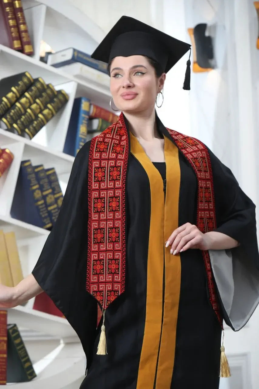 Woman wearing Palestinian graduation stole with traditional red embroidery and black tassels over black and gold graduation gown