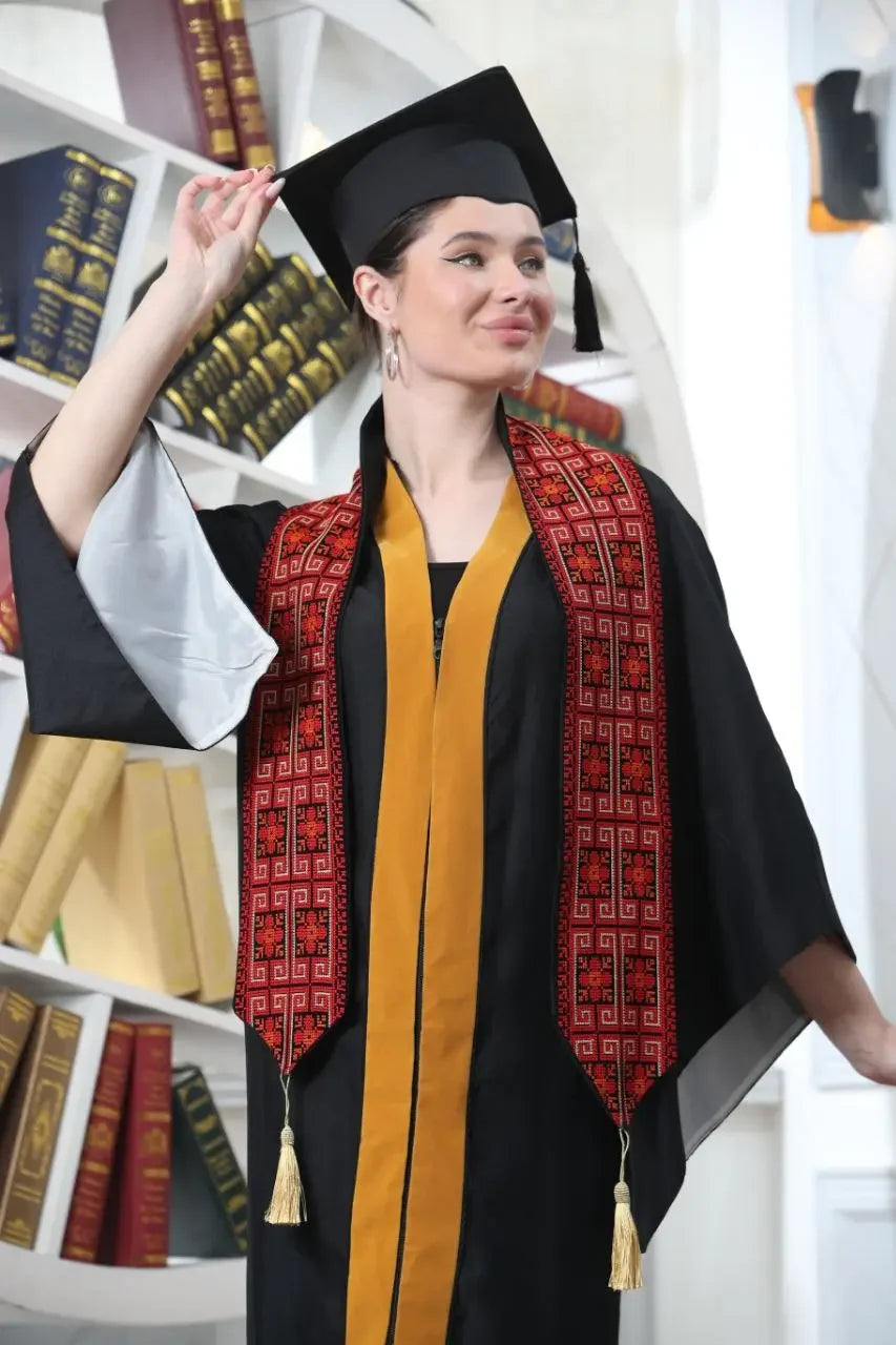 Woman wearing a Palestinian graduation stole in red and black with tassels over a graduation gown