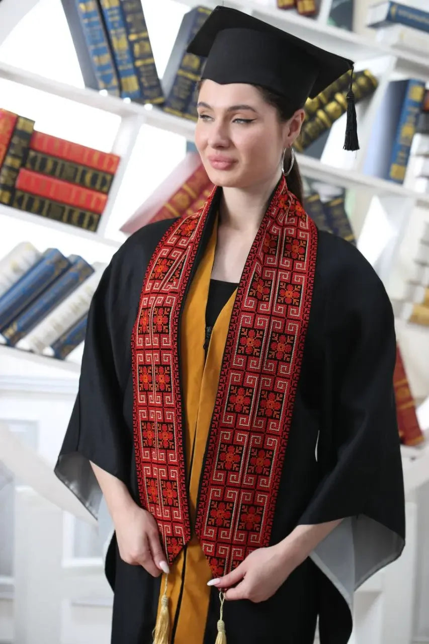 Woman wearing a Palestinian graduation stole with traditional red embroidery and black graduation gown and cap