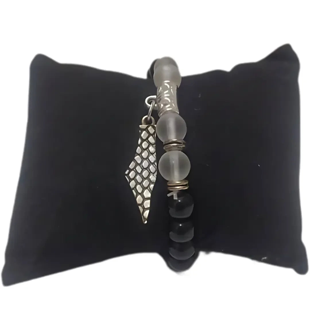 Palestinian silver bracelet with black and frosted beads and textured silver charm on black cushion