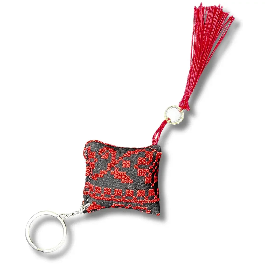 Palestinian tatreez keychains with red cross-stitch embroidery on black fabric and red tassel accessory