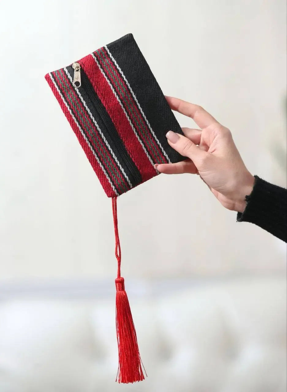 Hand holding a Palestinian wool wallet with red and black stripes and a red tassel accessory