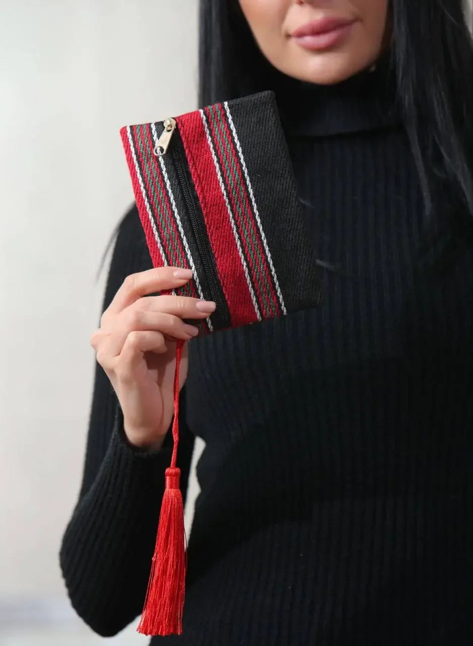 Woman holding a Palestinian wool wallet with red and black stripes and tassel accessory