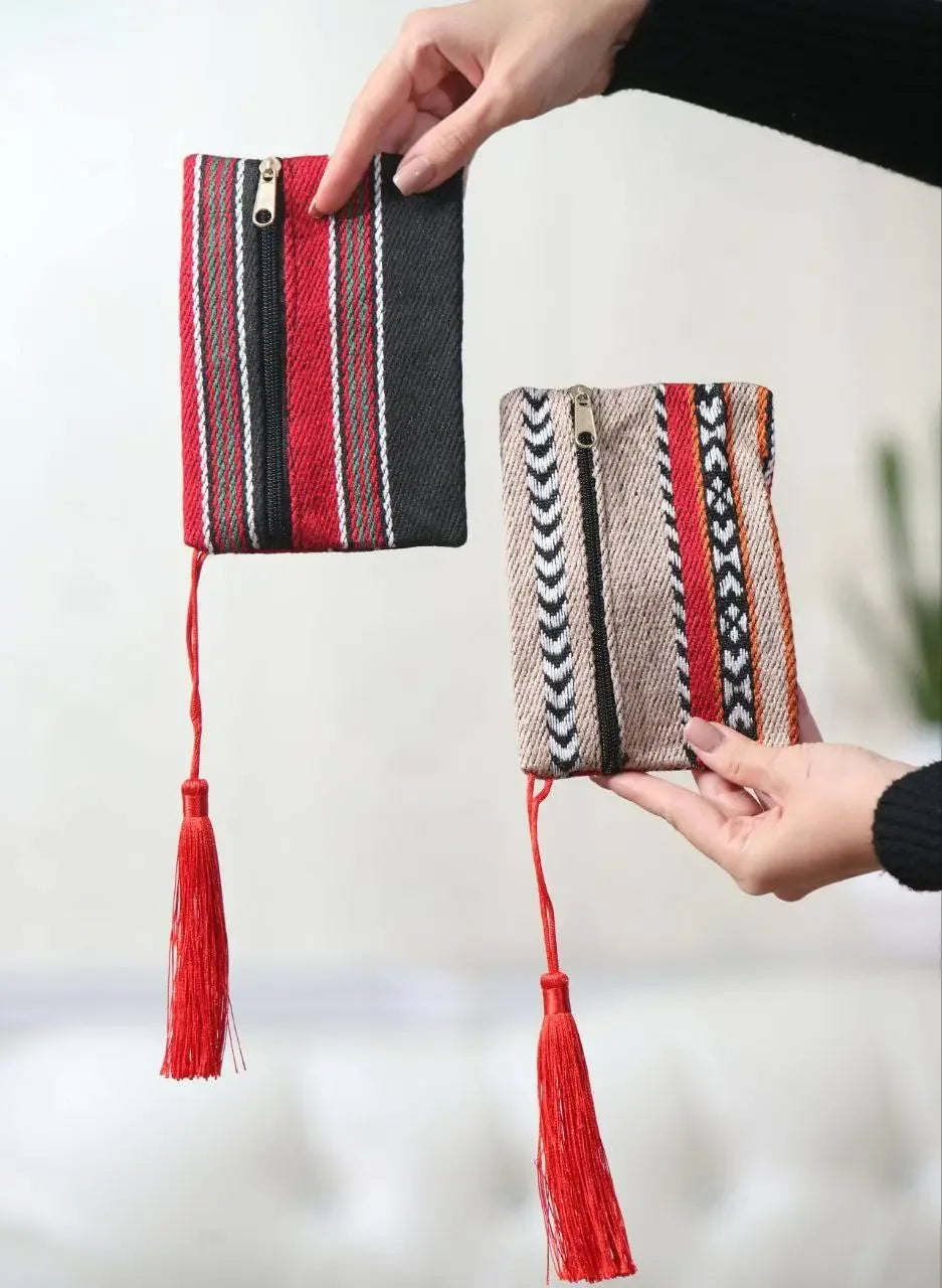 Hand holding two Palestinian wool wallets with traditional patterns and red tassels by Palestinian Elegance