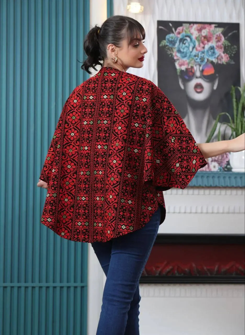 Palestinian embroidered cape in red with intricate traditional patterns worn casually by a woman indoors