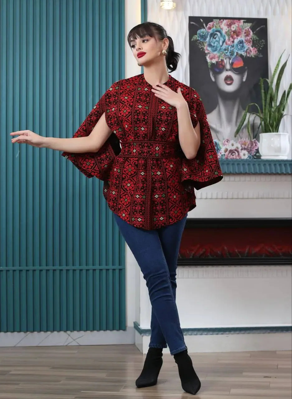 Palestinian embroidered cape from Palestinian Elegance worn by a woman styled with dark jeans and black boots