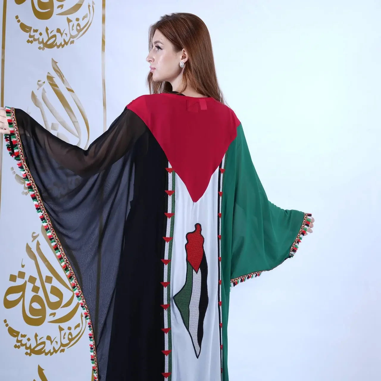 Woman wearing a Palestinian flag dress with black, red, white, and green colors and decorative tassels on sleeves