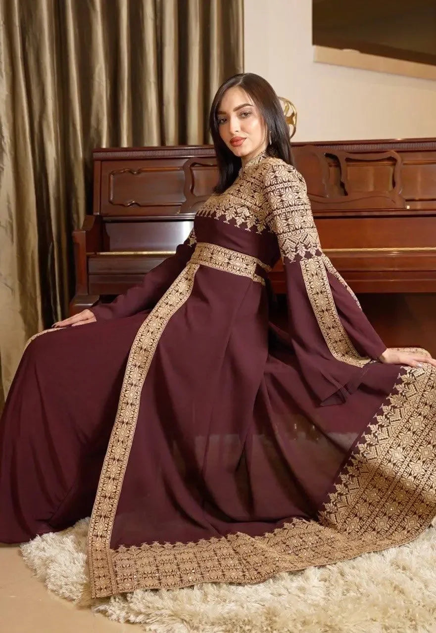 Palestinian Elegance maroon tatreez dress for women with intricate gold embroidery seated by piano