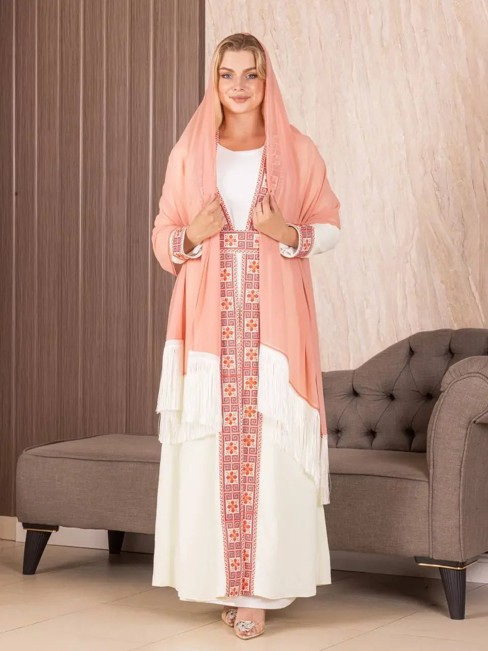 Woman wearing a traditional Palestinian khirka shawl in peach with embroidered patterns and white fringe