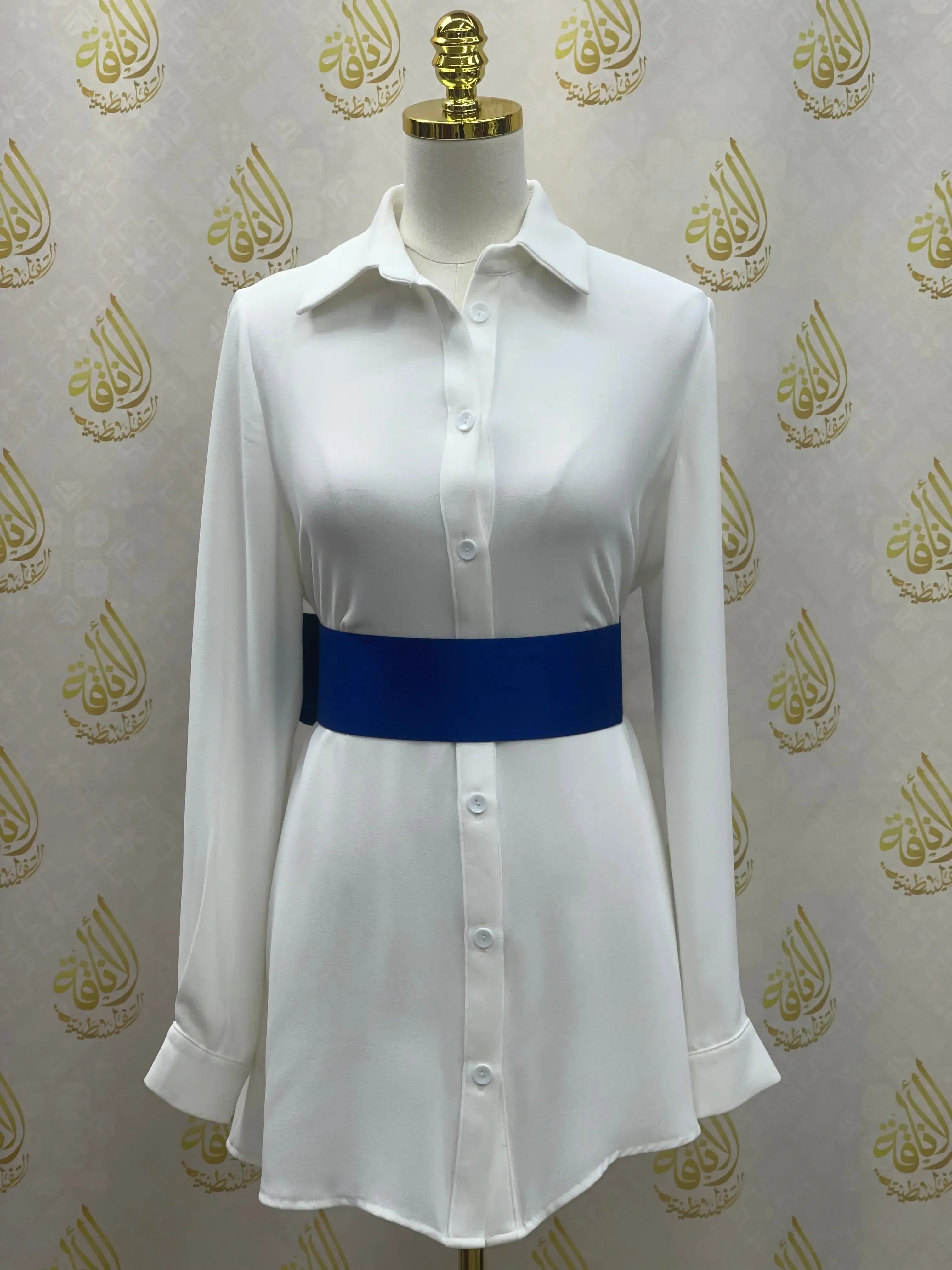 White button-down dress styled with a blue satin waist belt by Palestinian Elegance