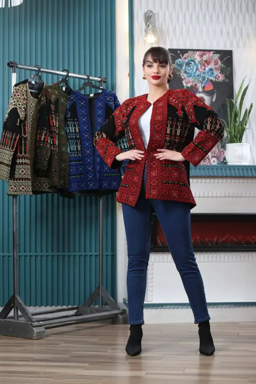 Woman wearing red tatreez embroidered jacket from Palestinian Elegance standing indoors with jackets on rack