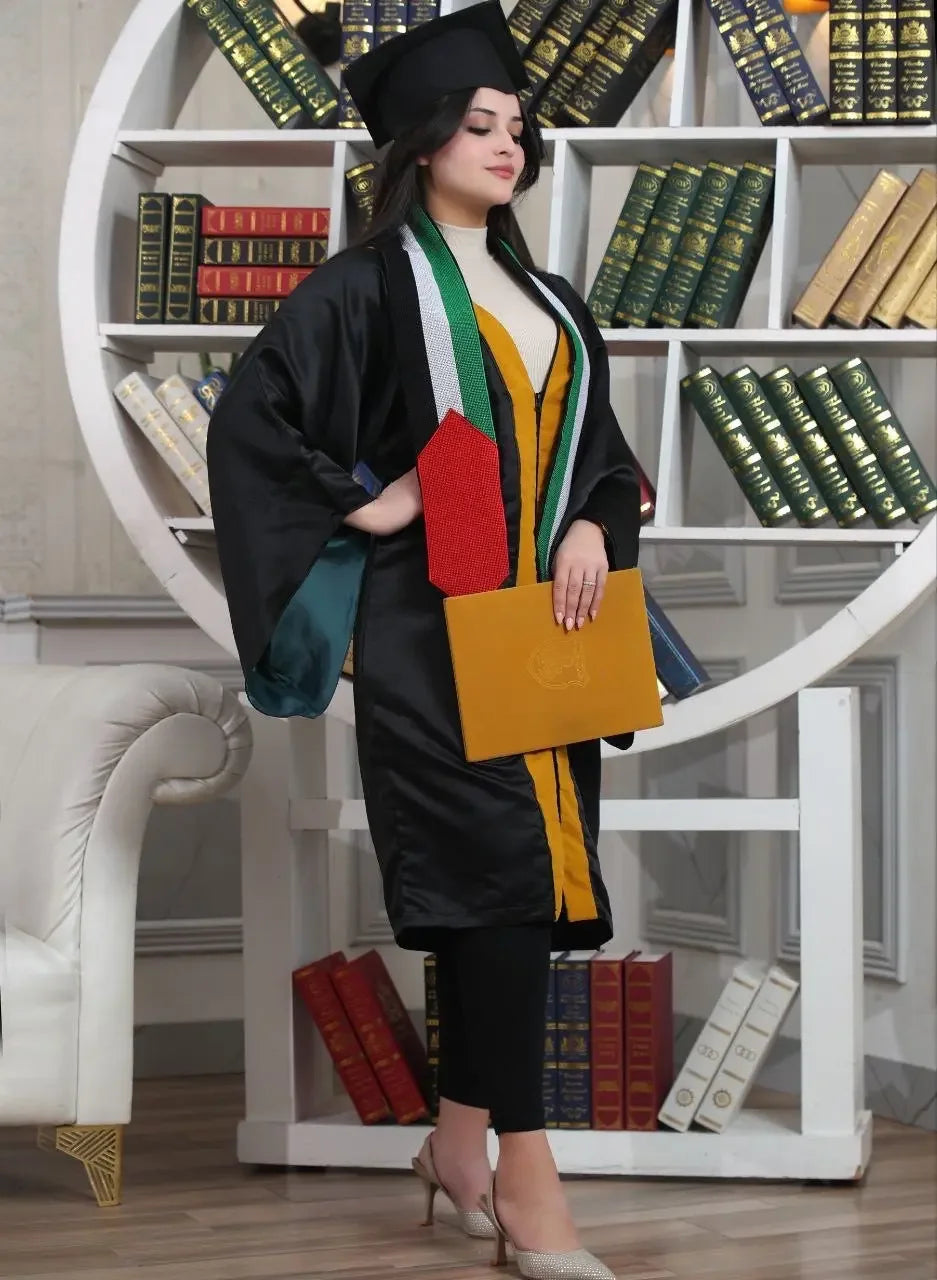 Graduate woman wearing tatreez stole with Palestinian flag over black gown holding diploma in library