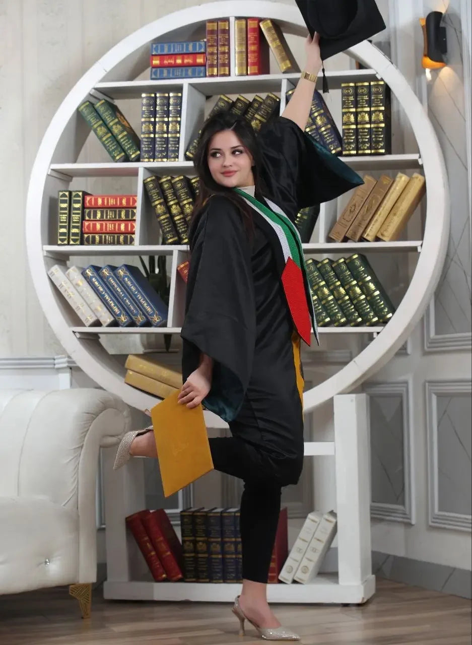 Woman wearing a tatreez stole with Palestinian flag over black graduation gown holding a cap and diploma