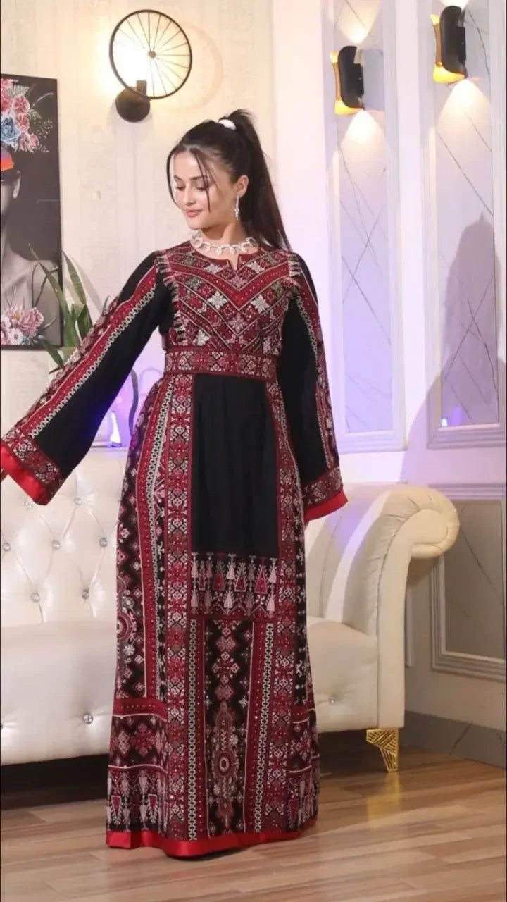 Woman wearing a traditional embroidered thoub with intricate red and black Palestinian designs indoors