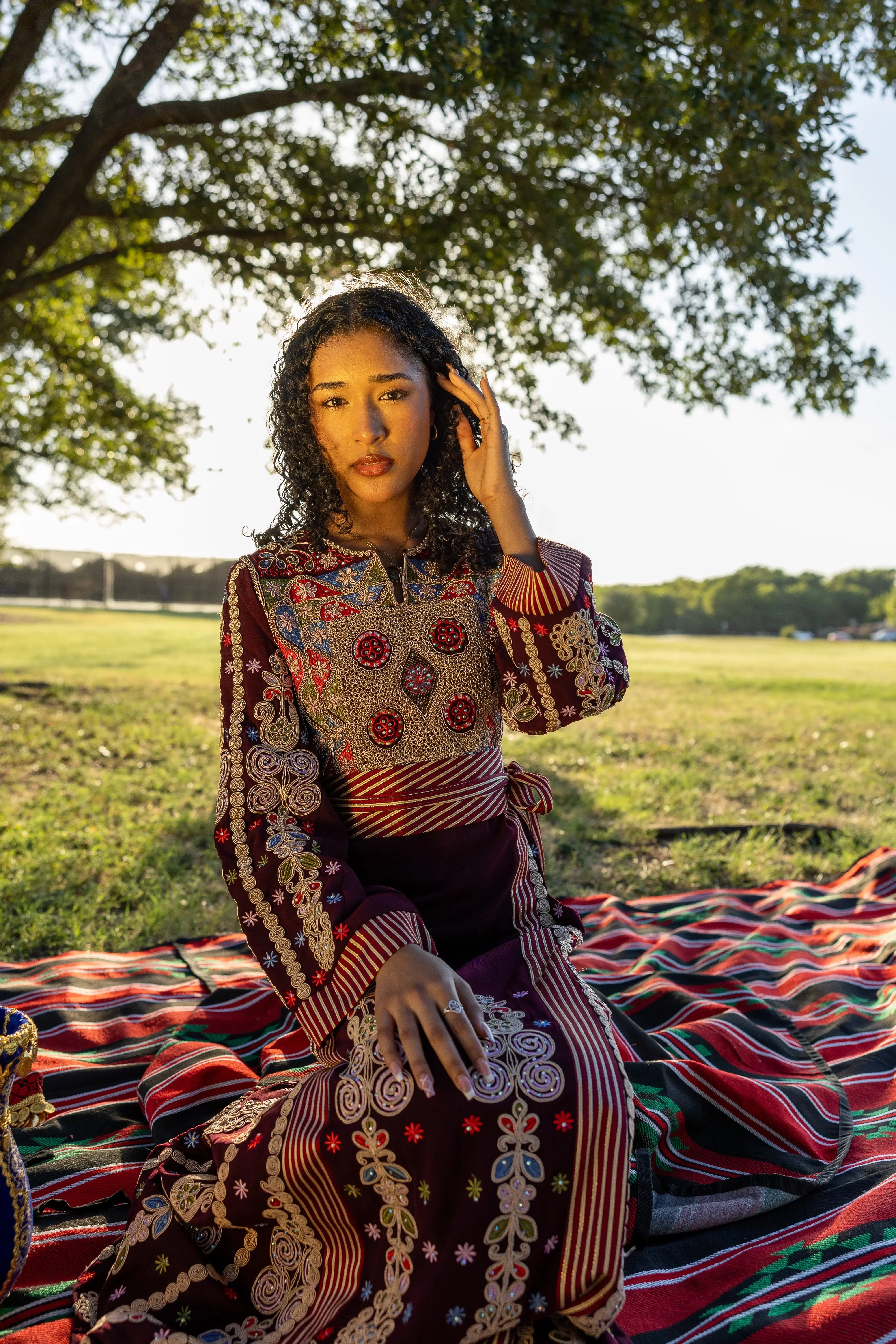 Woman wearing traditional Palestinian thoub embroidery dress sitting outdoors on patterned fabric blanket