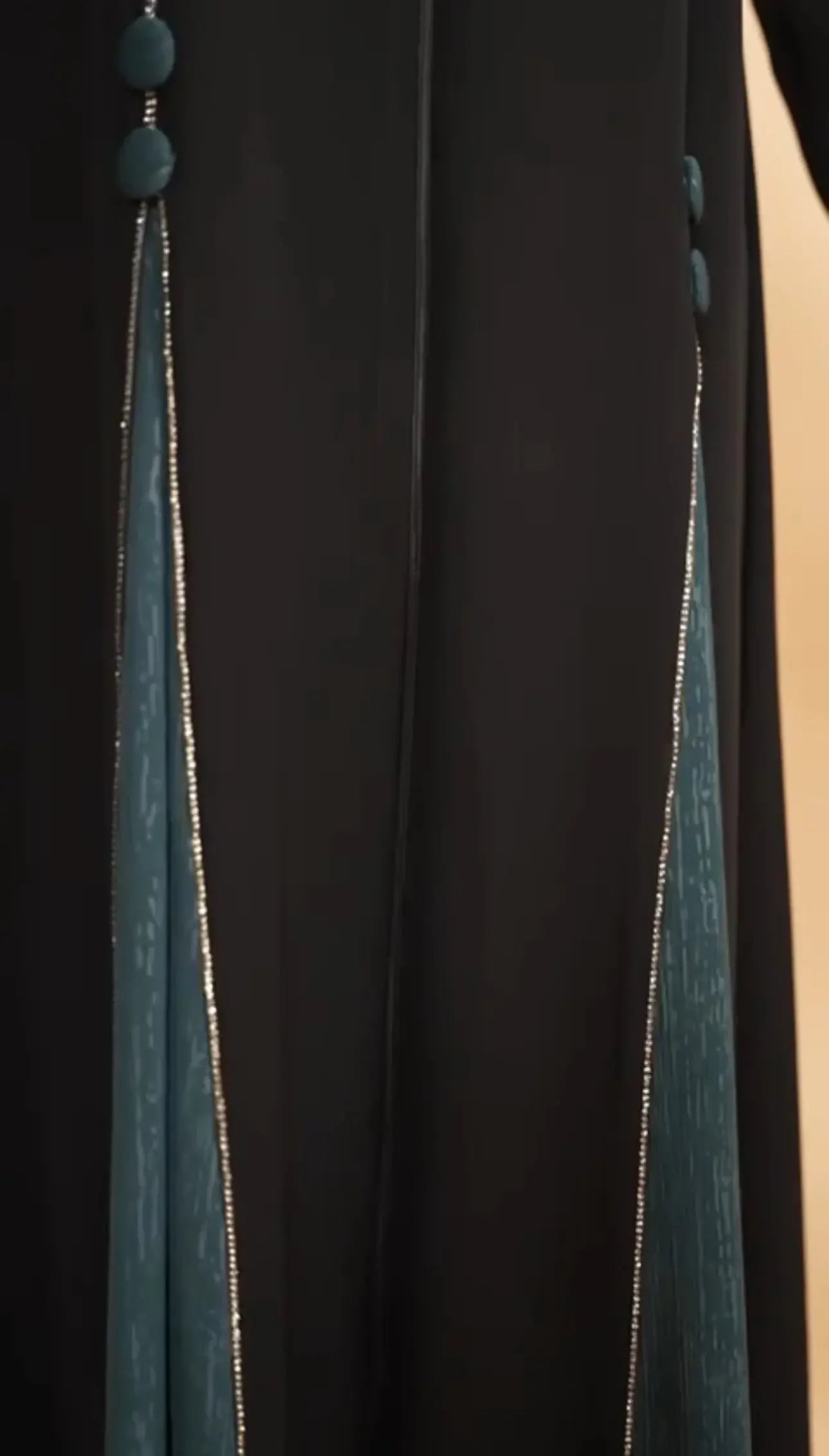 Close-up of Palestinian Elegance elegant abaya for women with black fabric and teal side panels embellished with gold trim