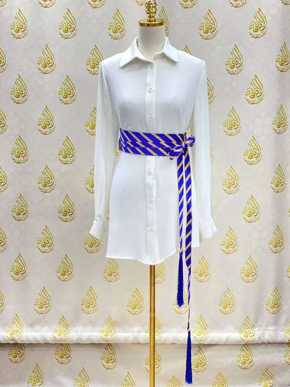 White button-down dress styled with a blue and gold embroidered kashmir belt by Palestinian Elegance