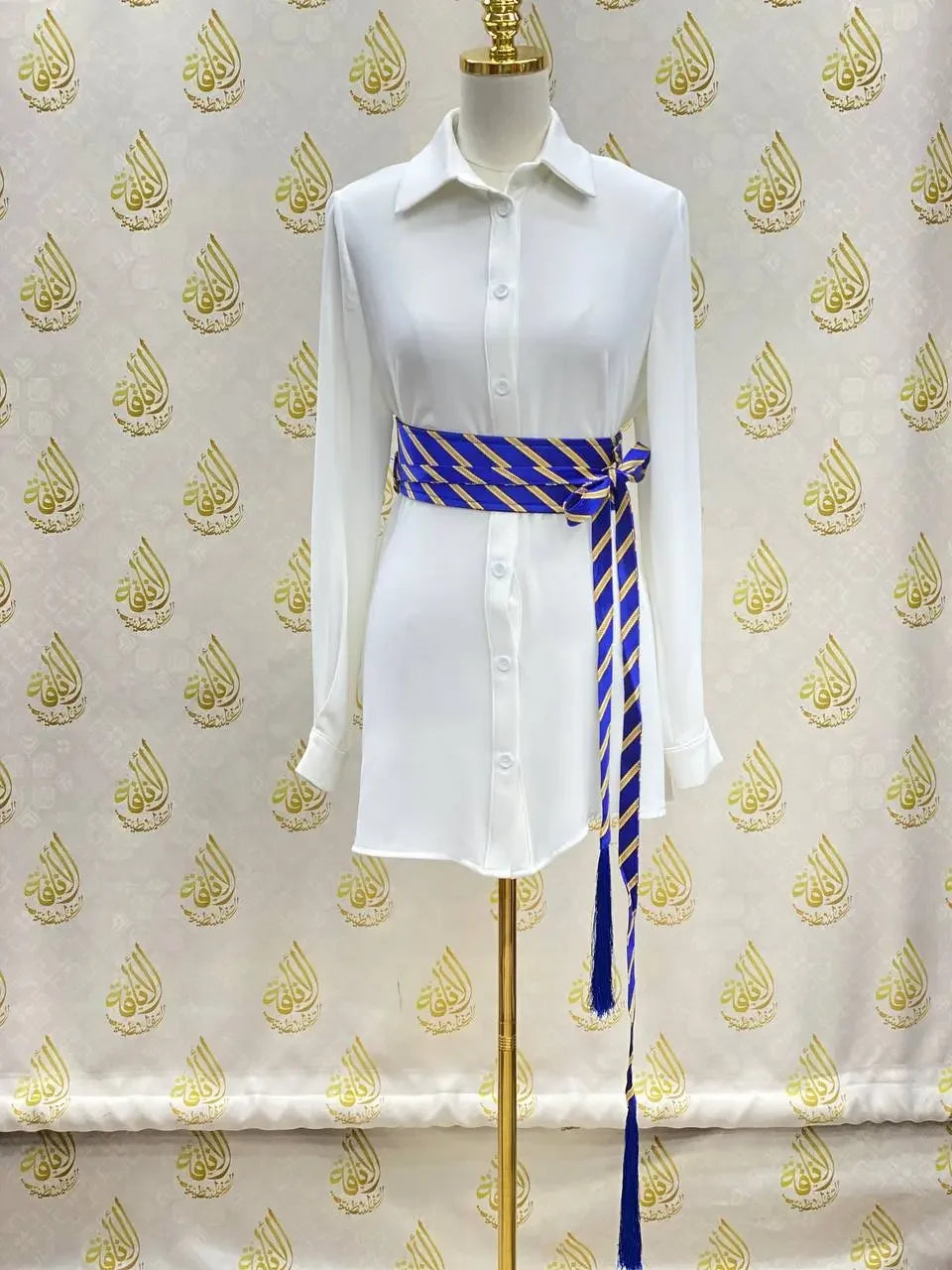 Embroidered kashmir belt in blue and gold wrapped around a white button-up dress on a mannequin