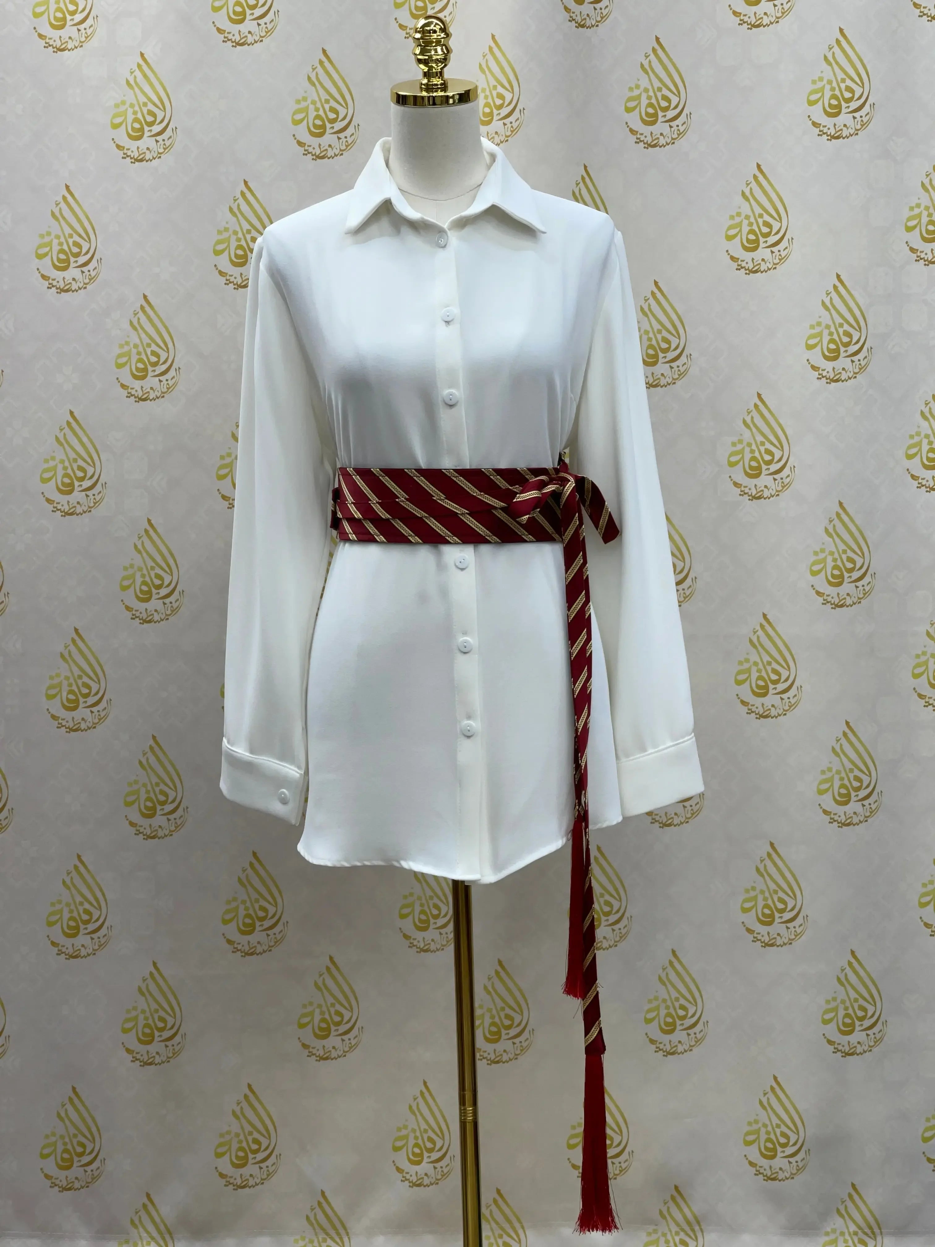 White button-down shirt styled with a red and beige embroidered kashmir belt tied at the waist