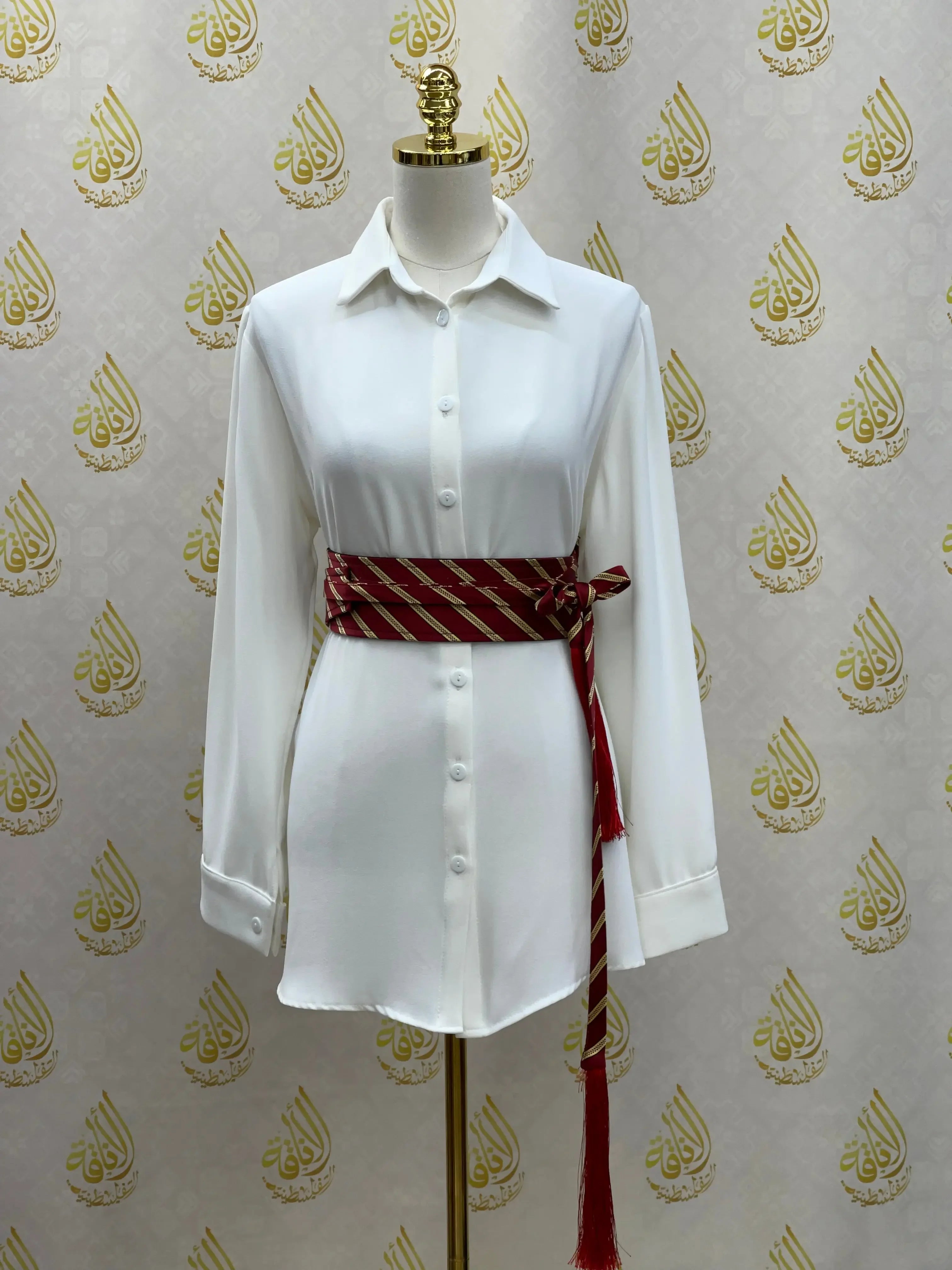 Embroidered kashmir belt in red and gold worn over white button-up shirt on mannequin