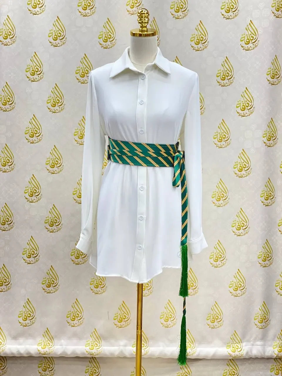 Embroidered kashmir belt in green and gold wrapped around a white shirt dress on a mannequin