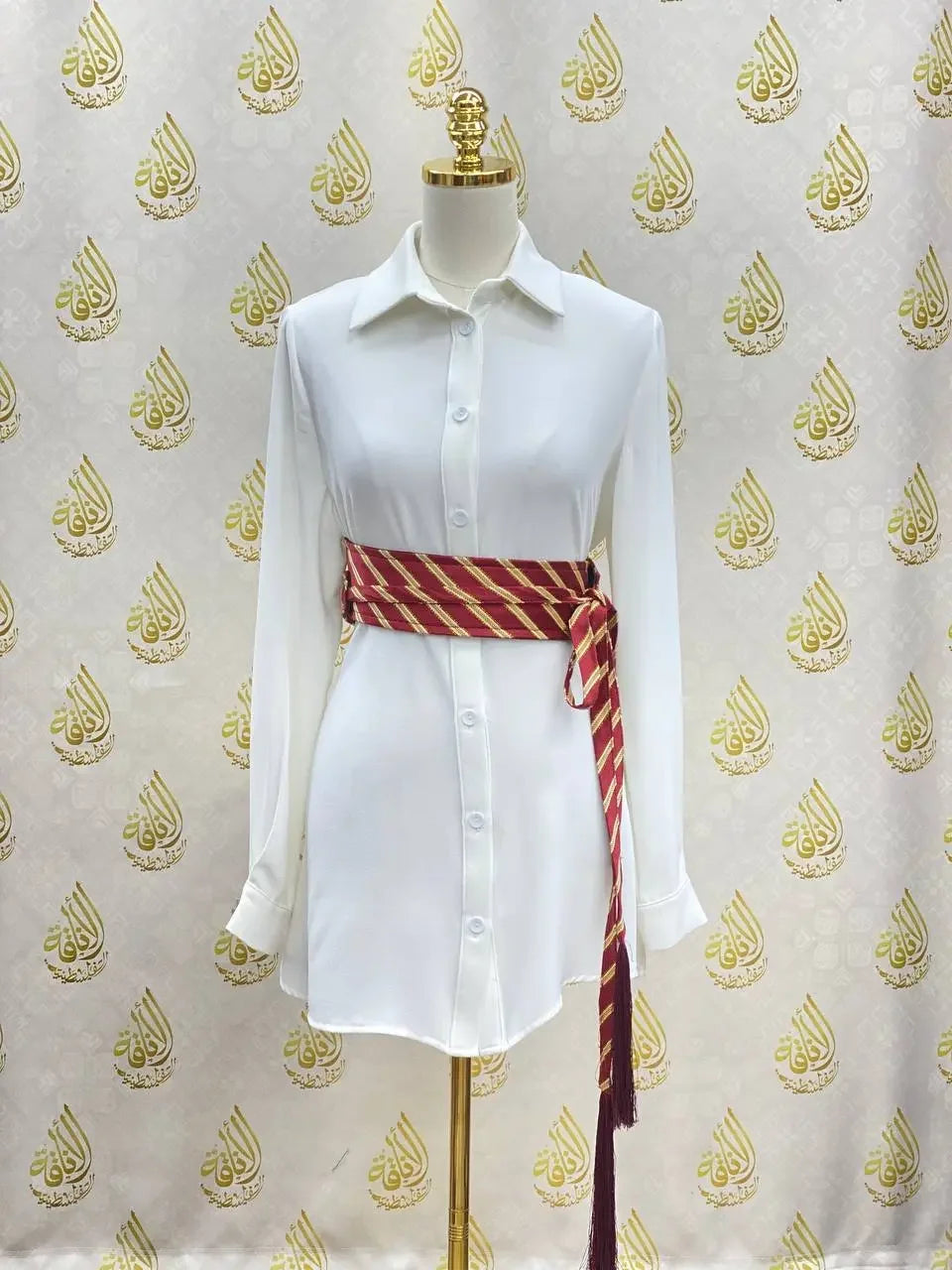 White button-down shirt dress styled with a red and gold embroidered kashmir belt by Palestinian Elegance