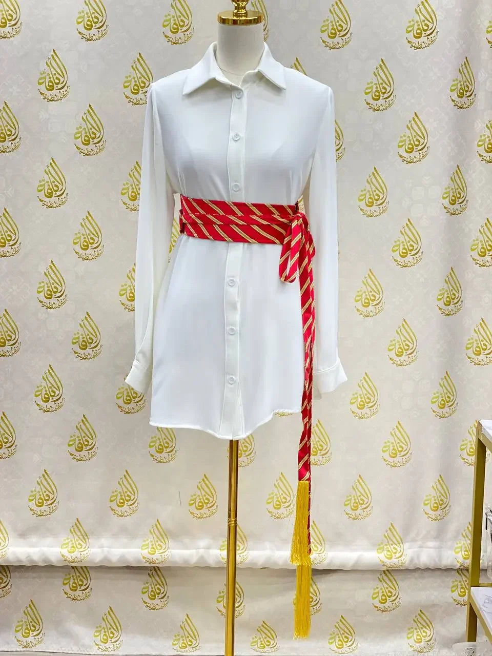 Embroidered kashmir belt in red and gold wrapped around white shirt dress on mannequin
