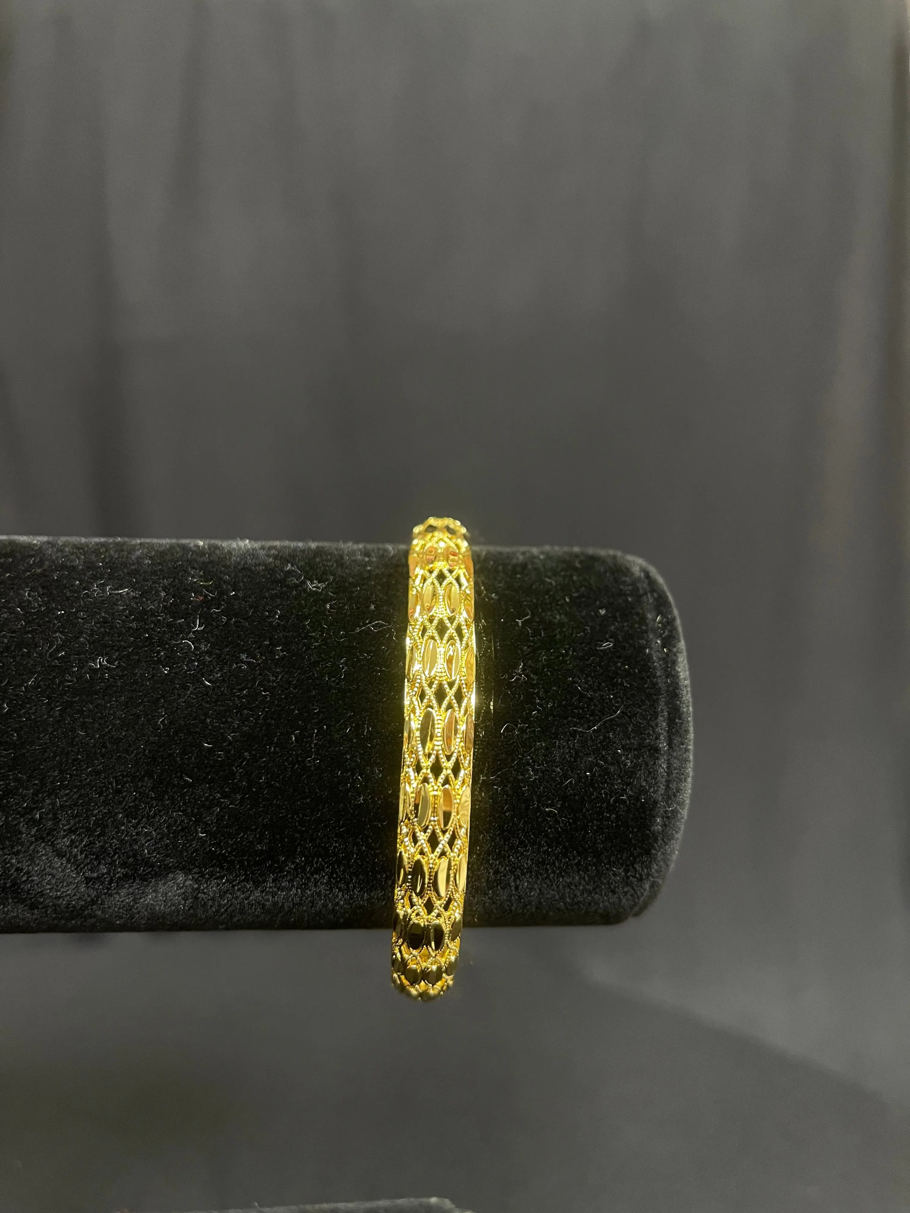 Palestinian Elegance imitation gold bangle bracelet with intricate lattice design on black display