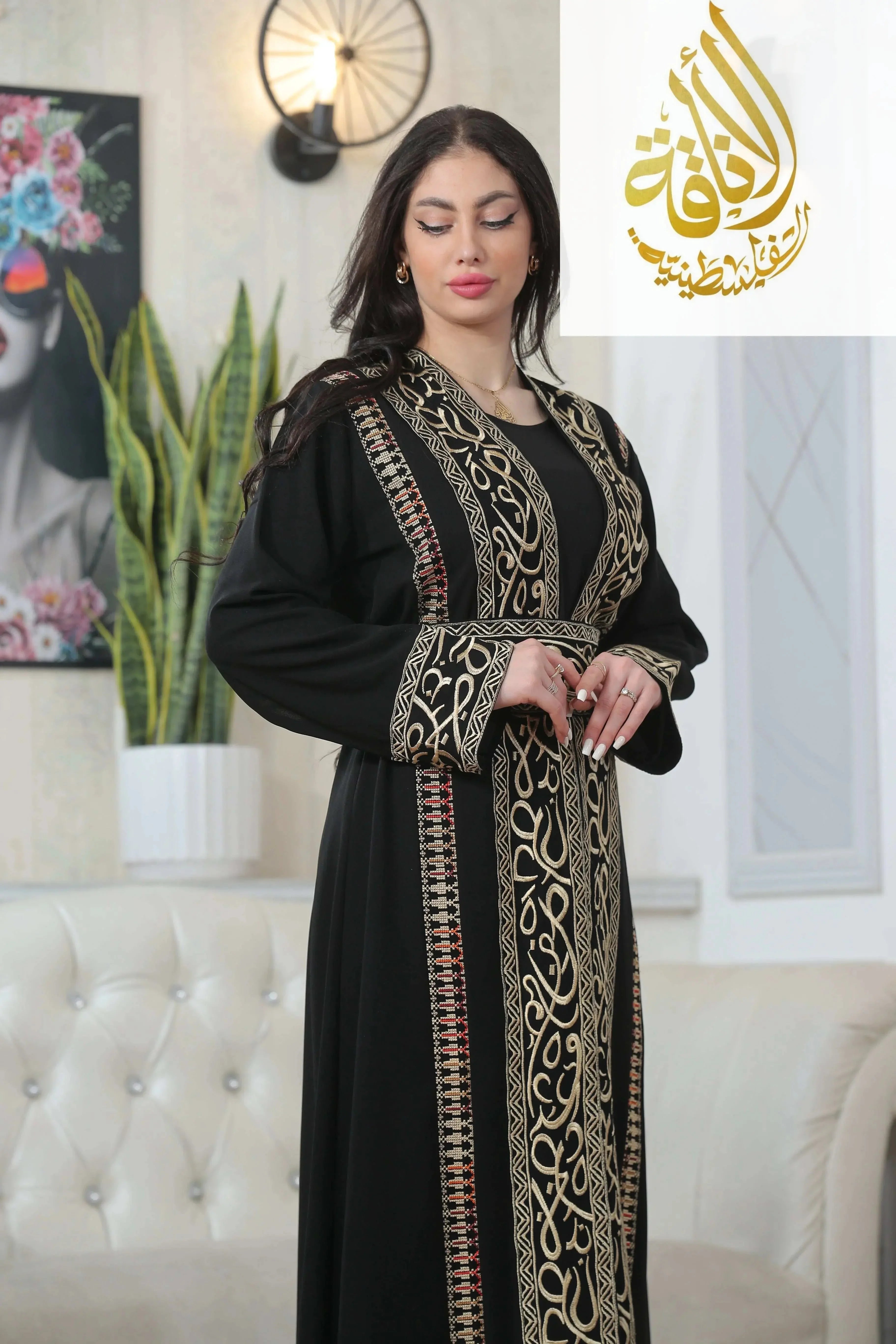Basma Arabic letters with heritage embroidery Bisht black thoub by Palestinian Elegance worn by a woman indoors