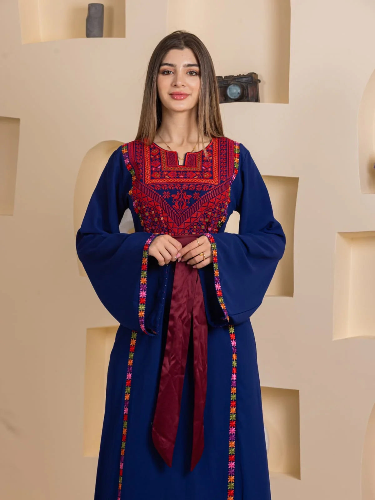 Woman modeling Blossom Embroidered Thobe in navy blue with red chest embroidery bell sleeves and burgundy sash