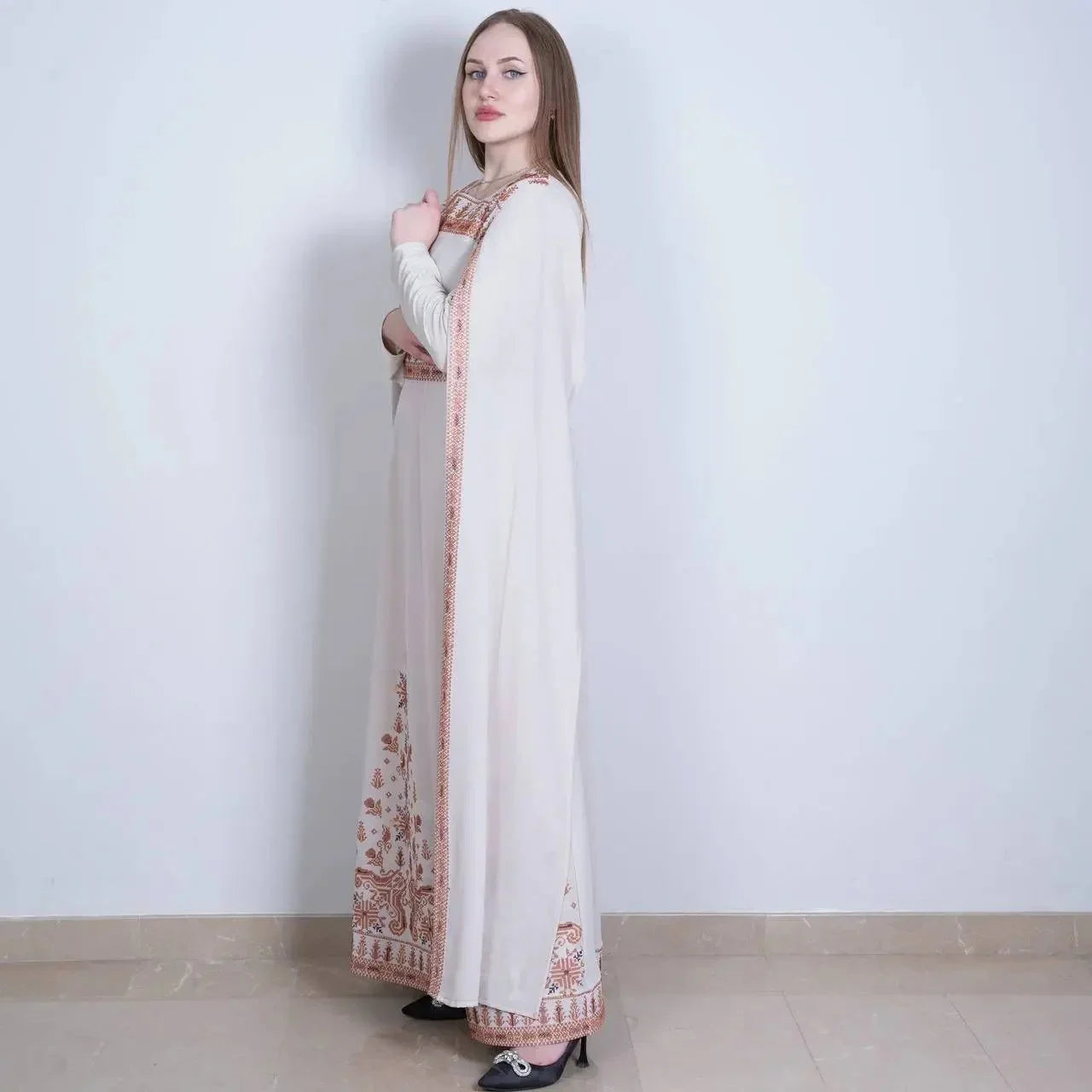 Woman wearing a long white embroidered Palestinian dress with intricate orange floral patterns
