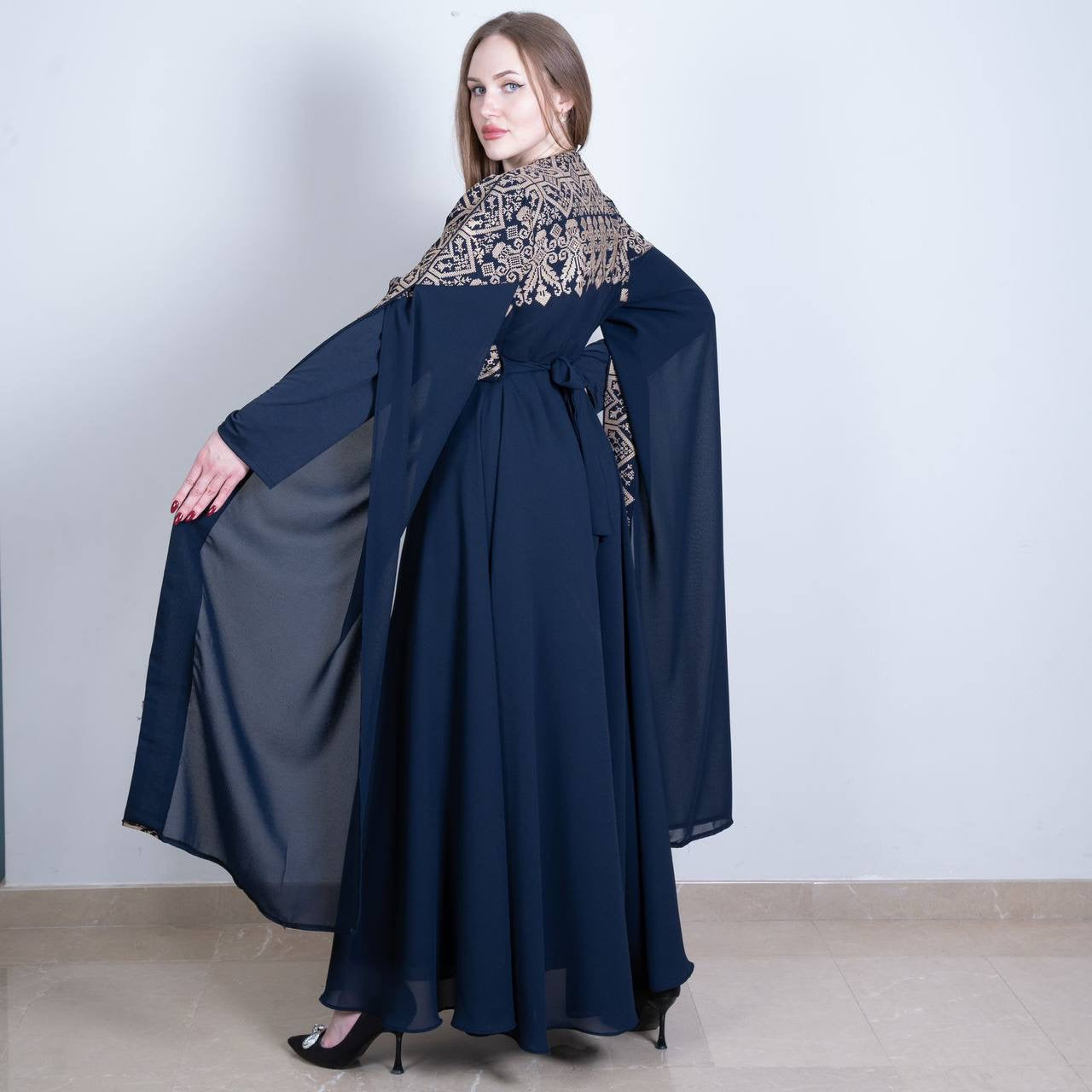 Woman wearing a navy blue Palestinian embroidered dress with intricate gold patterns and flowing sleeves