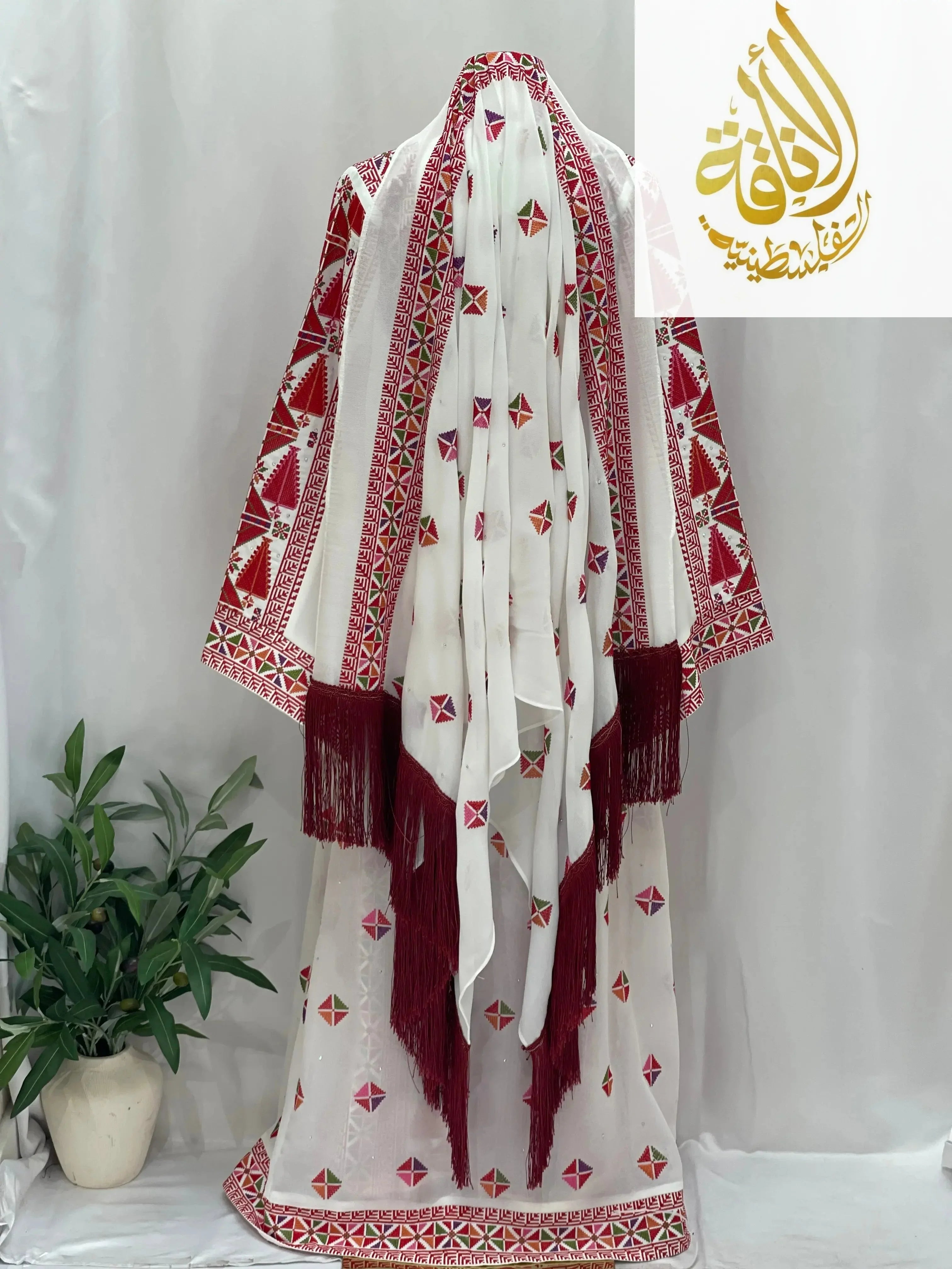 Embroidered Falahi thoub with overskirt by Palestinian Elegance featuring traditional red and white patterns with fringe details