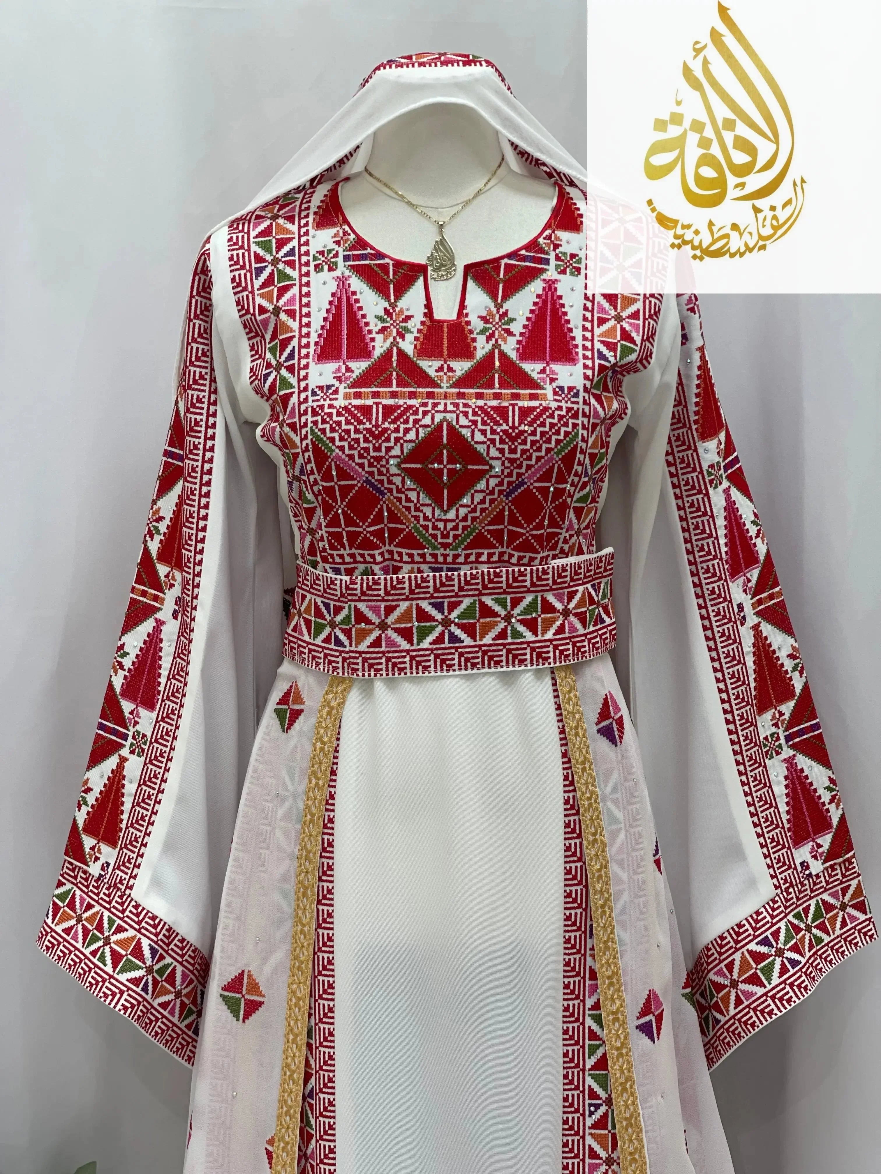 Embroidered Falahi thoub with overskirt by Palestinian Elegance featuring red and white geometric patterns