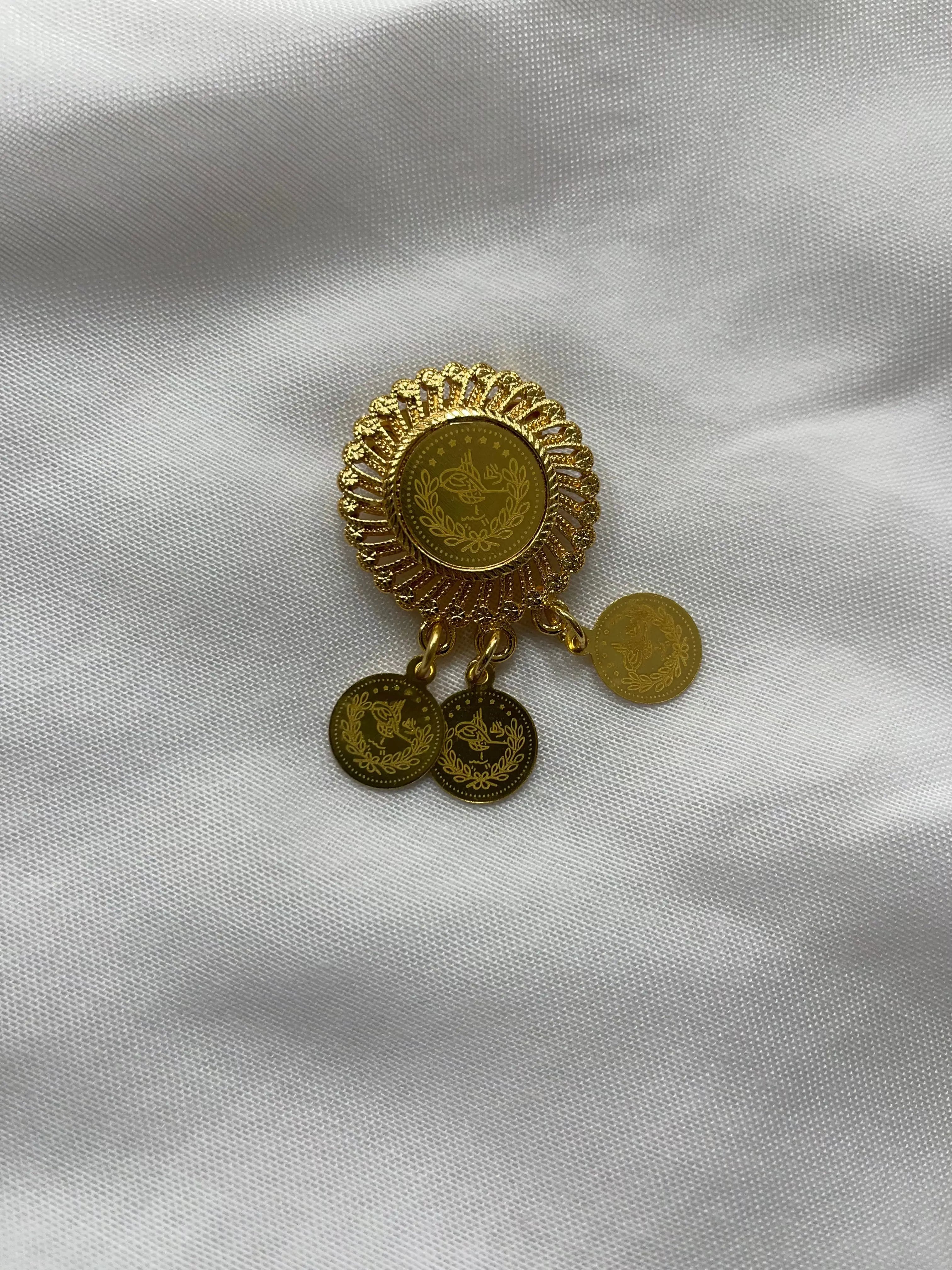 Palestinian Elegance imitation gold lapel pin with intricate coin design on white fabric background