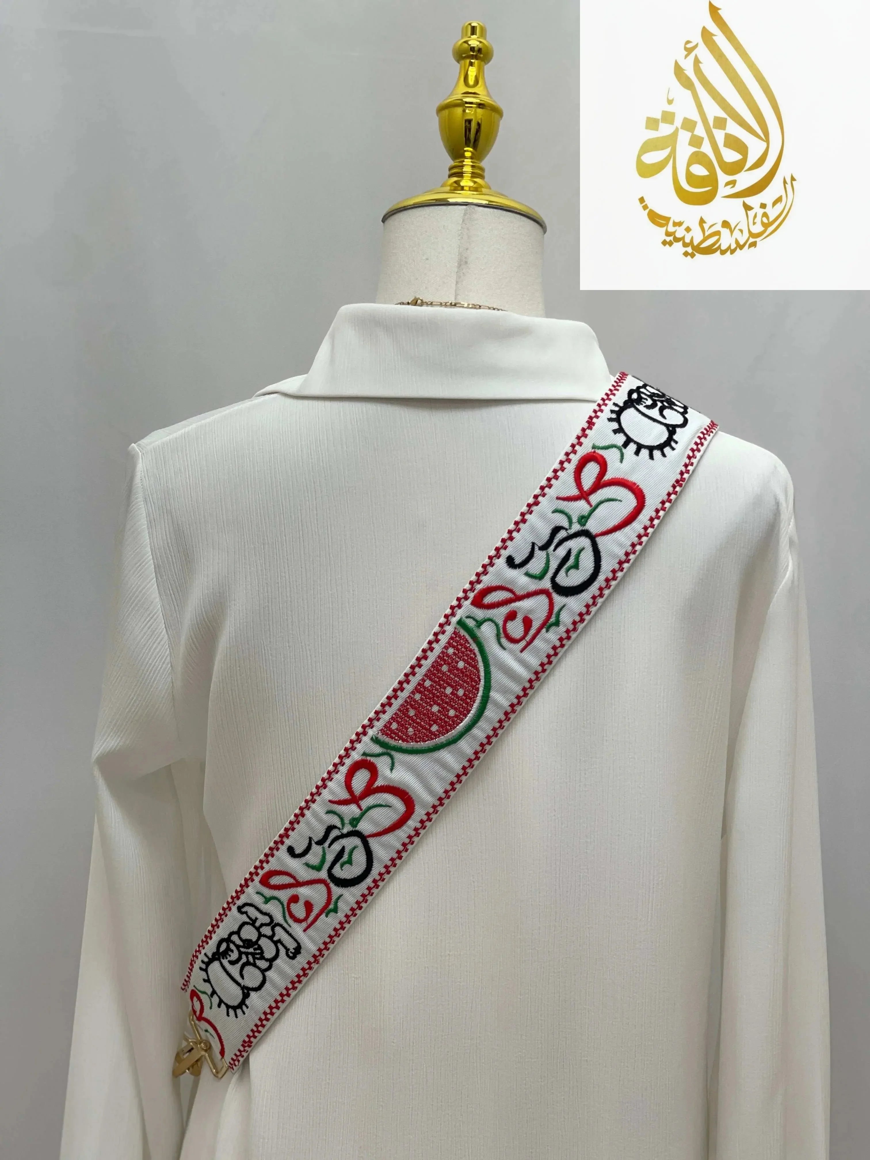 Palestinian embroidered purse strap with red, green, and black traditional designs displayed on white fabric