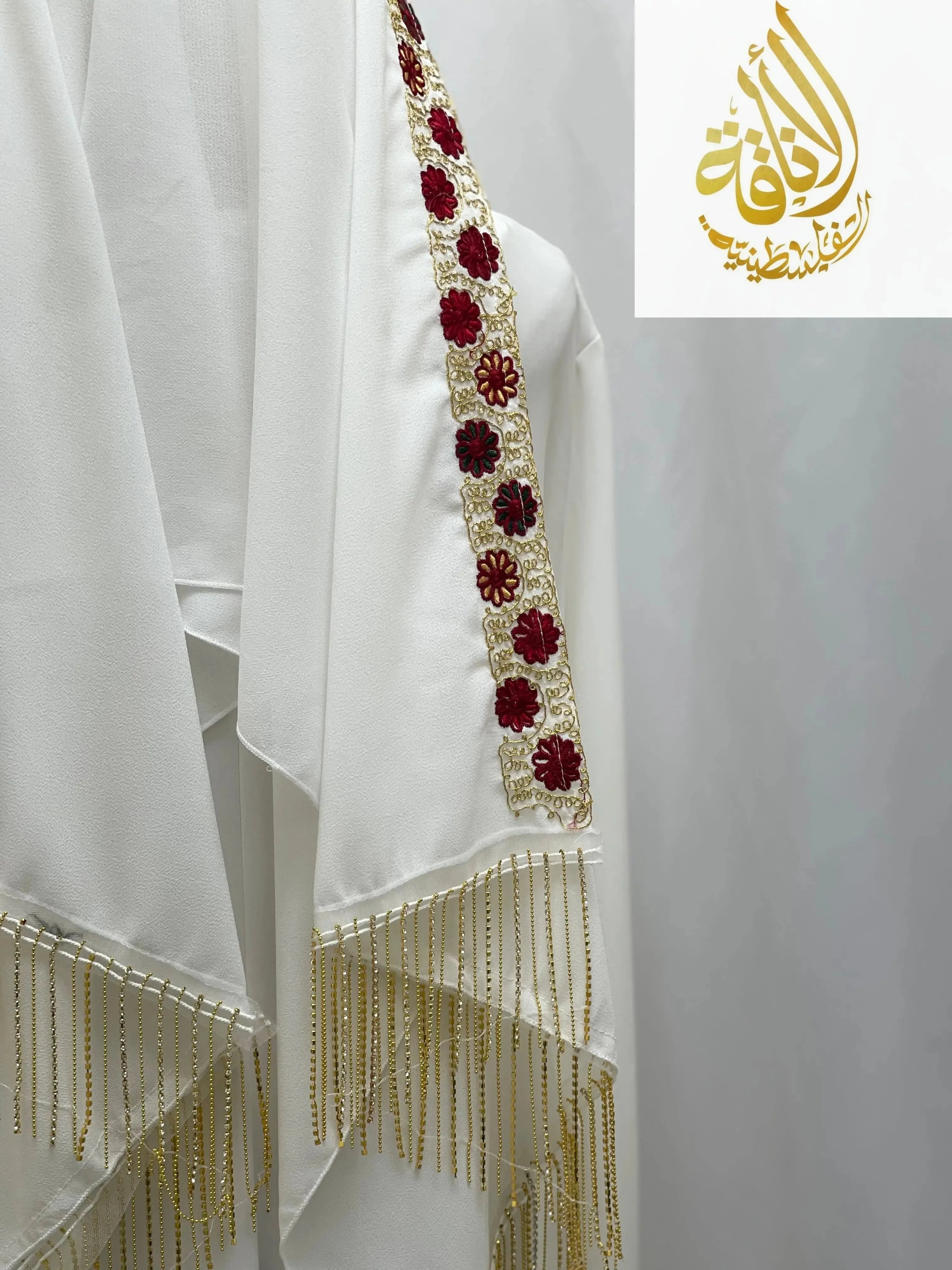 White embroidered fabric with red and gold floral detailing and gold fringe Palestinian Traditional Modest Fashion Kasab Khirka