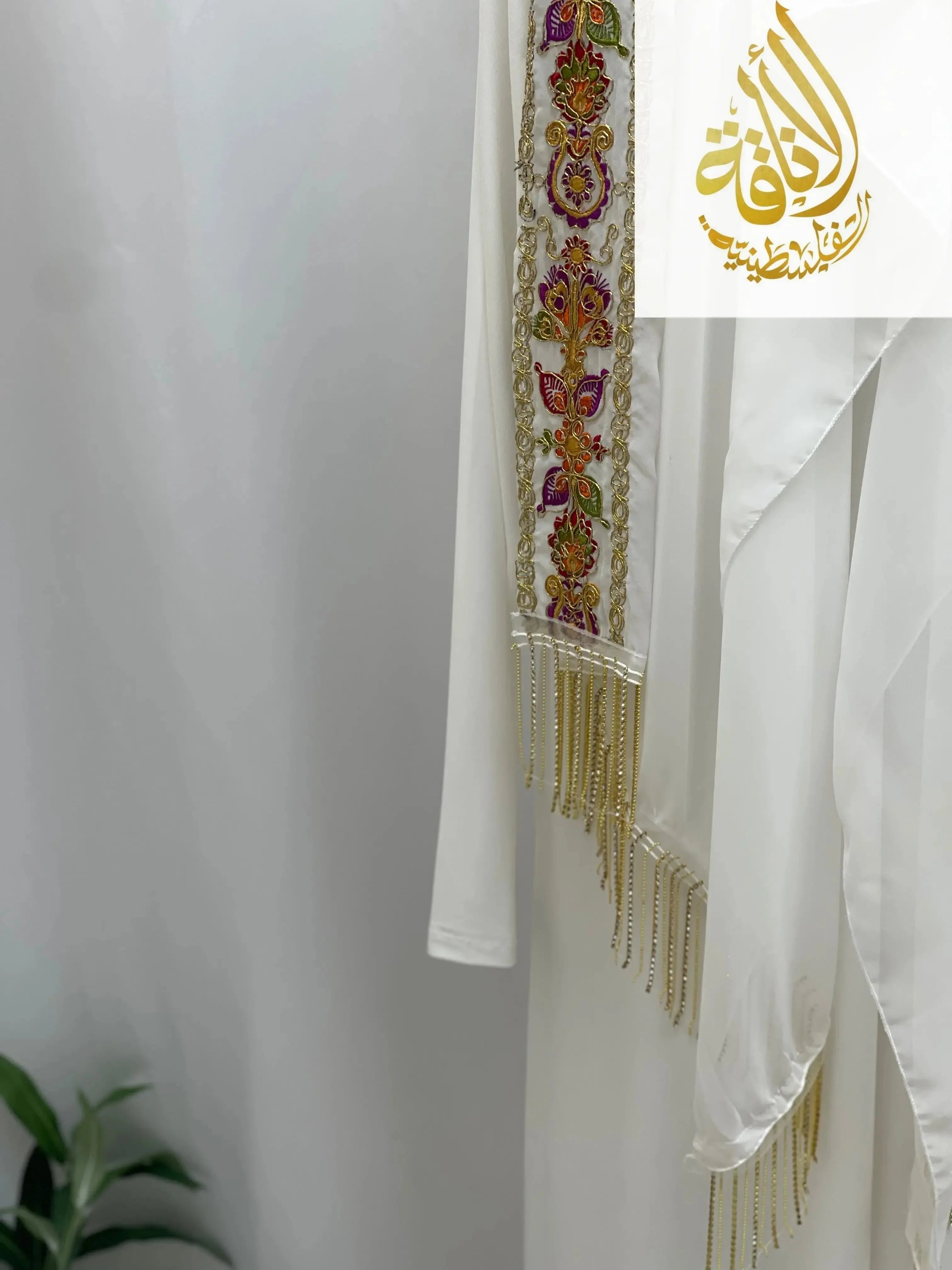 White embroidery detail with colorful floral patterns and gold fringe on Palestinian Traditional Modest Fashion Kasab Khirka