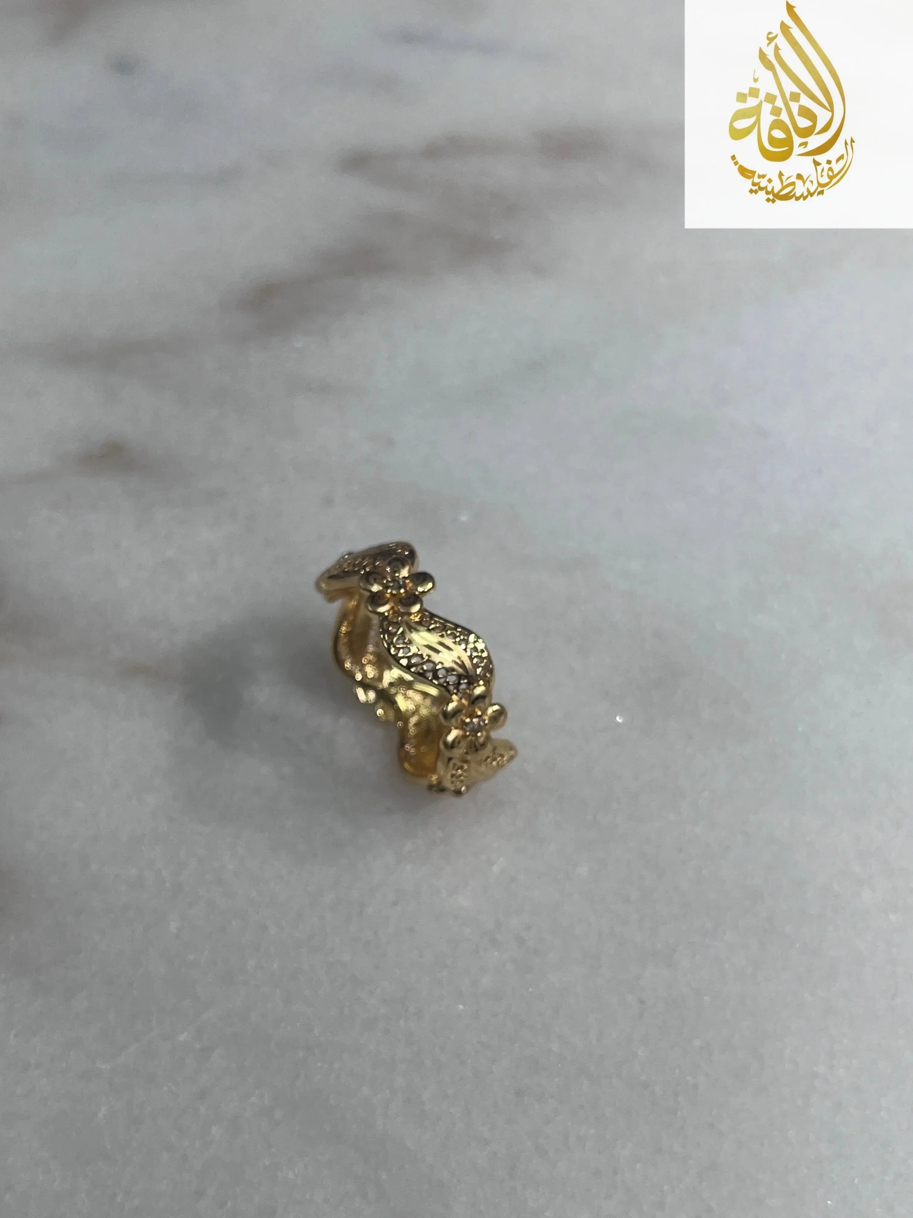 Imitated Gold Curved Ring with Flower Design by Palestinian Elegance on a marble surface