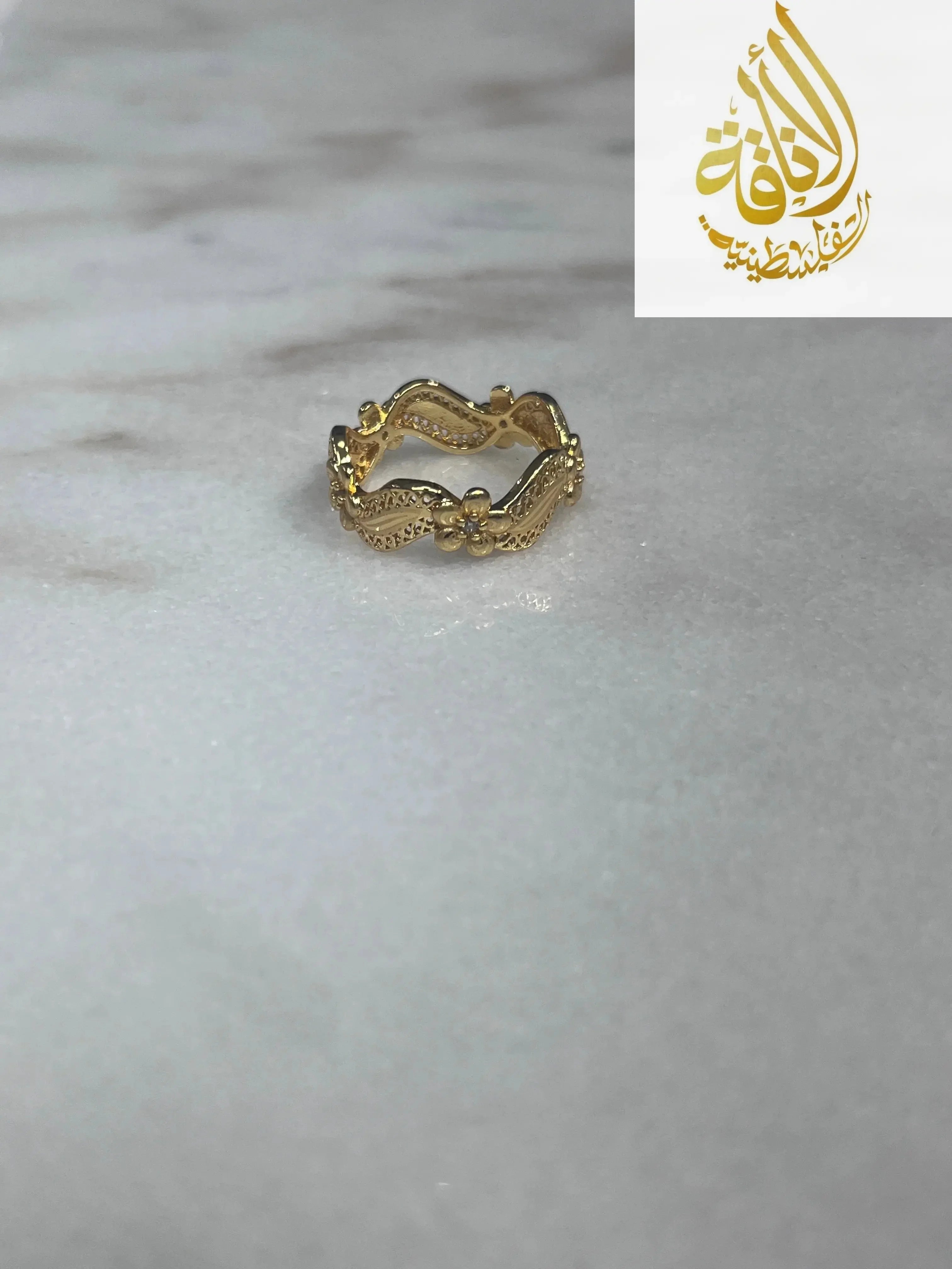 Imitated Gold Curved Ring with Flower Design by Palestinian Elegance on marble surface