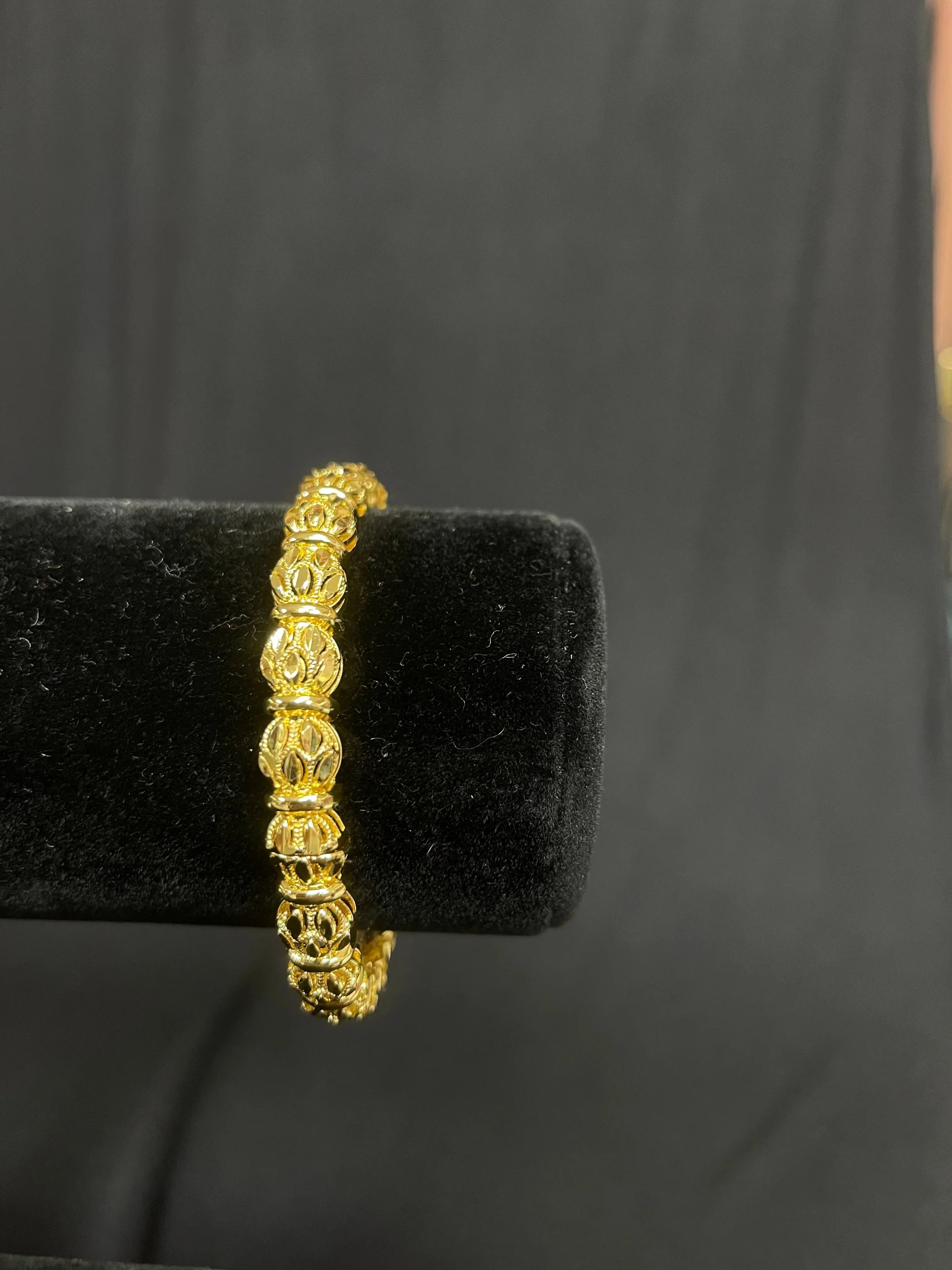 Kawther Bangle in imitated gold by Palestinian Elegance with intricate floral design on black display