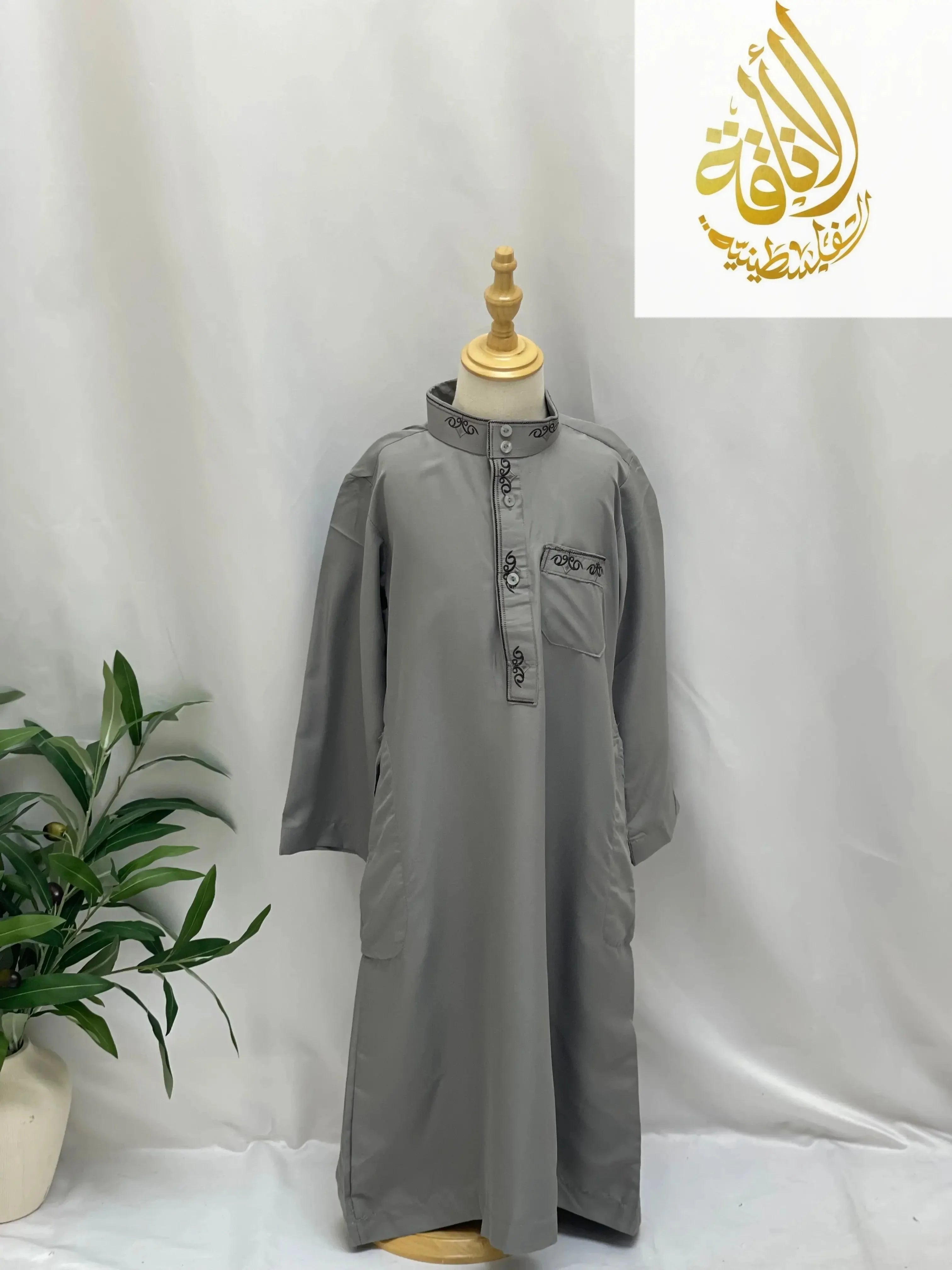 Gray kids embroidered thobe from Palestinian Elegance with long sleeves and button details on mannequin