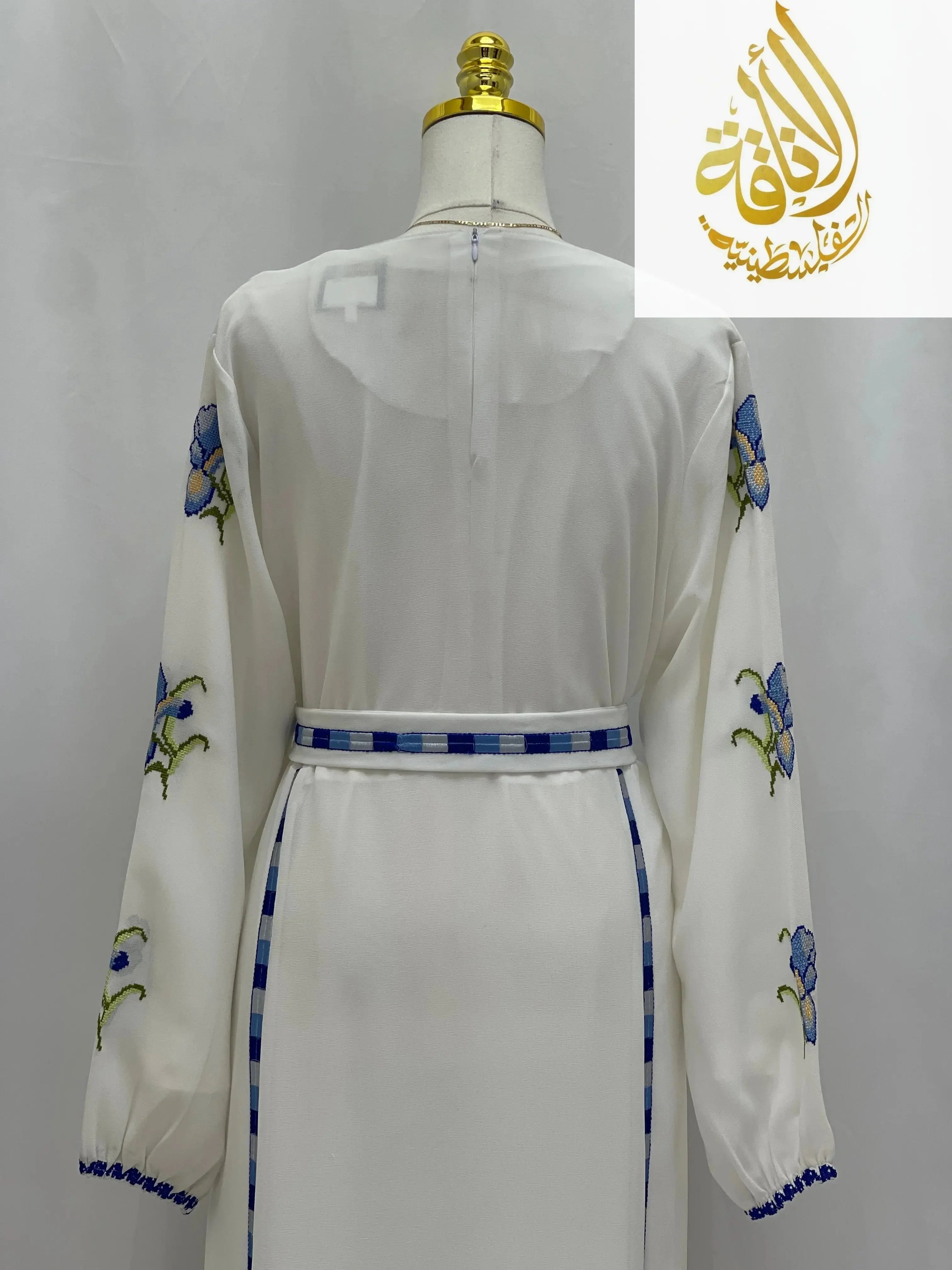 Back view of a white Palestinian embroidered dress with blue floral embroidery and checkered belt detail