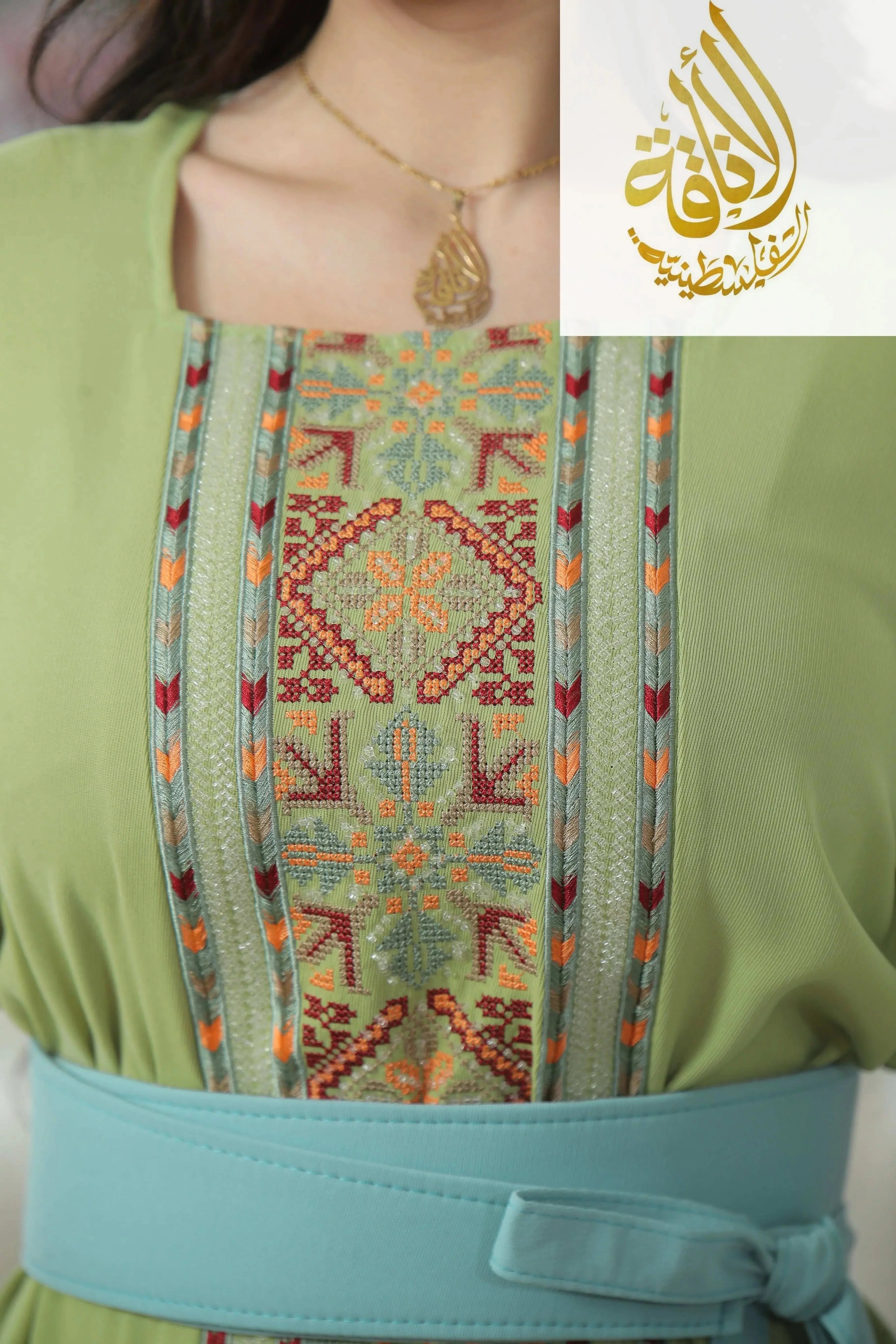 Close-up of Nadera Embroidered Thoub by Palestinian Elegance featuring intricate multicolor embroidery on green fabric with blue belt